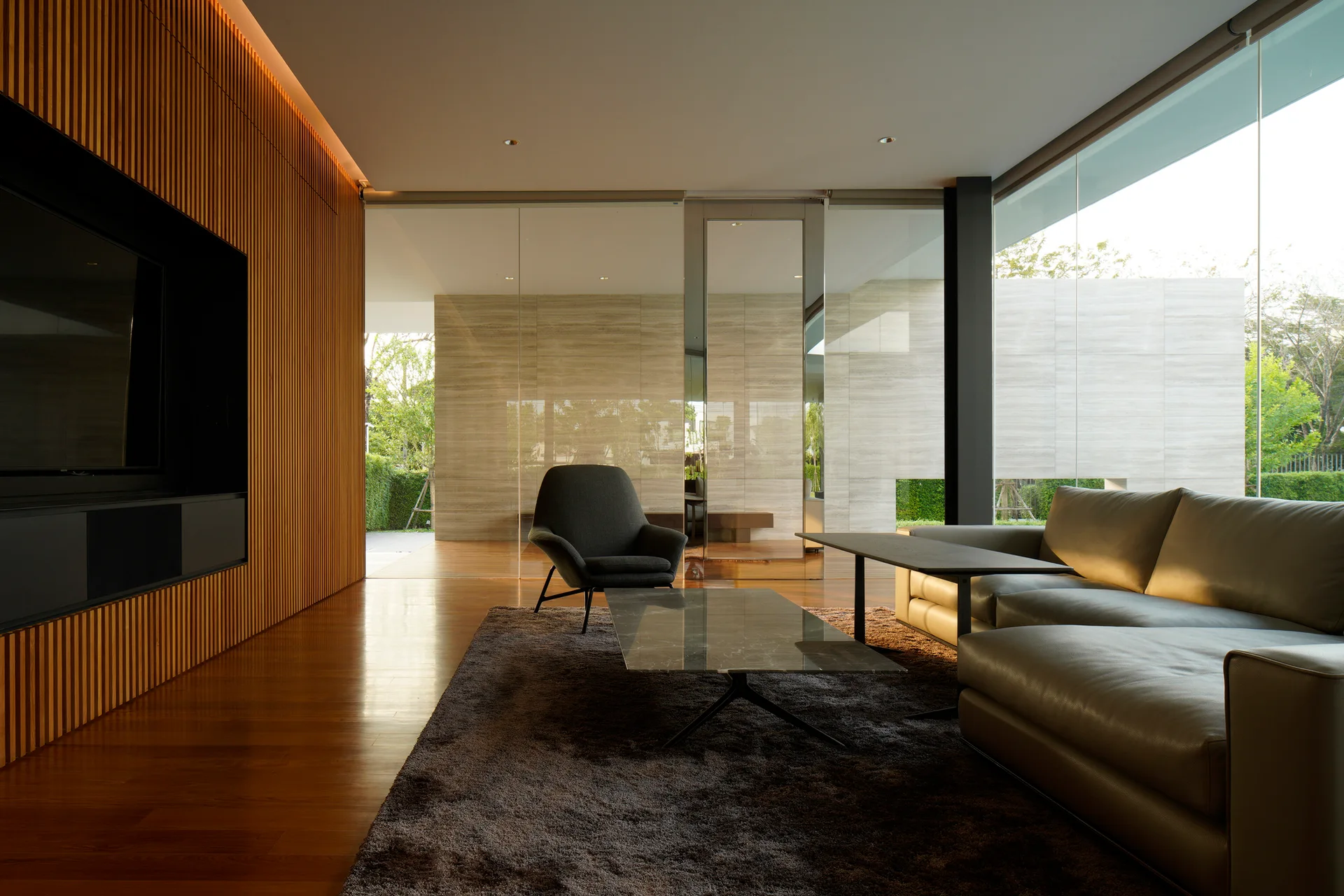 A minimalist living room features a leather sectional sofa, a marble-topped coffee table, and a vertical wood-slat feature wall next to large glass panels.