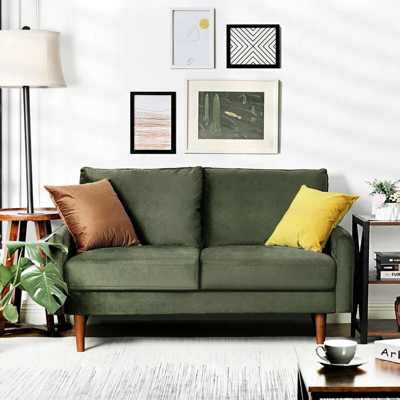 An olive green velvet loveseat with tapered wooden legs sits against a white wall decorated with four small framed art prints.