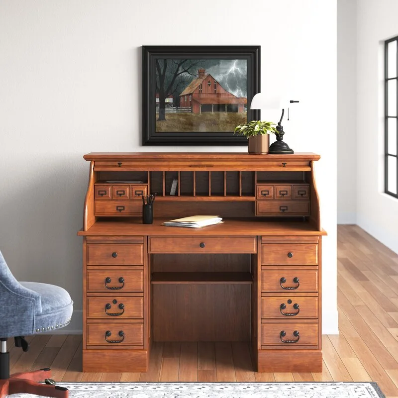 A traditional wooden roll-top desk with built-in pigeonholes and drawers stands on a hardwood floor under a framed painting.