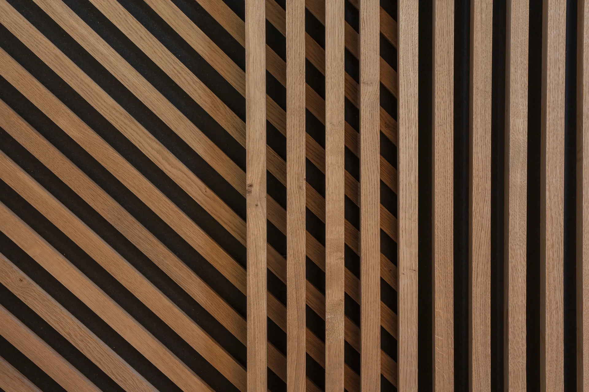 A close-up of wall paneling featuring light brown vertical wood slats layered over a diagonal slat pattern against a dark background.