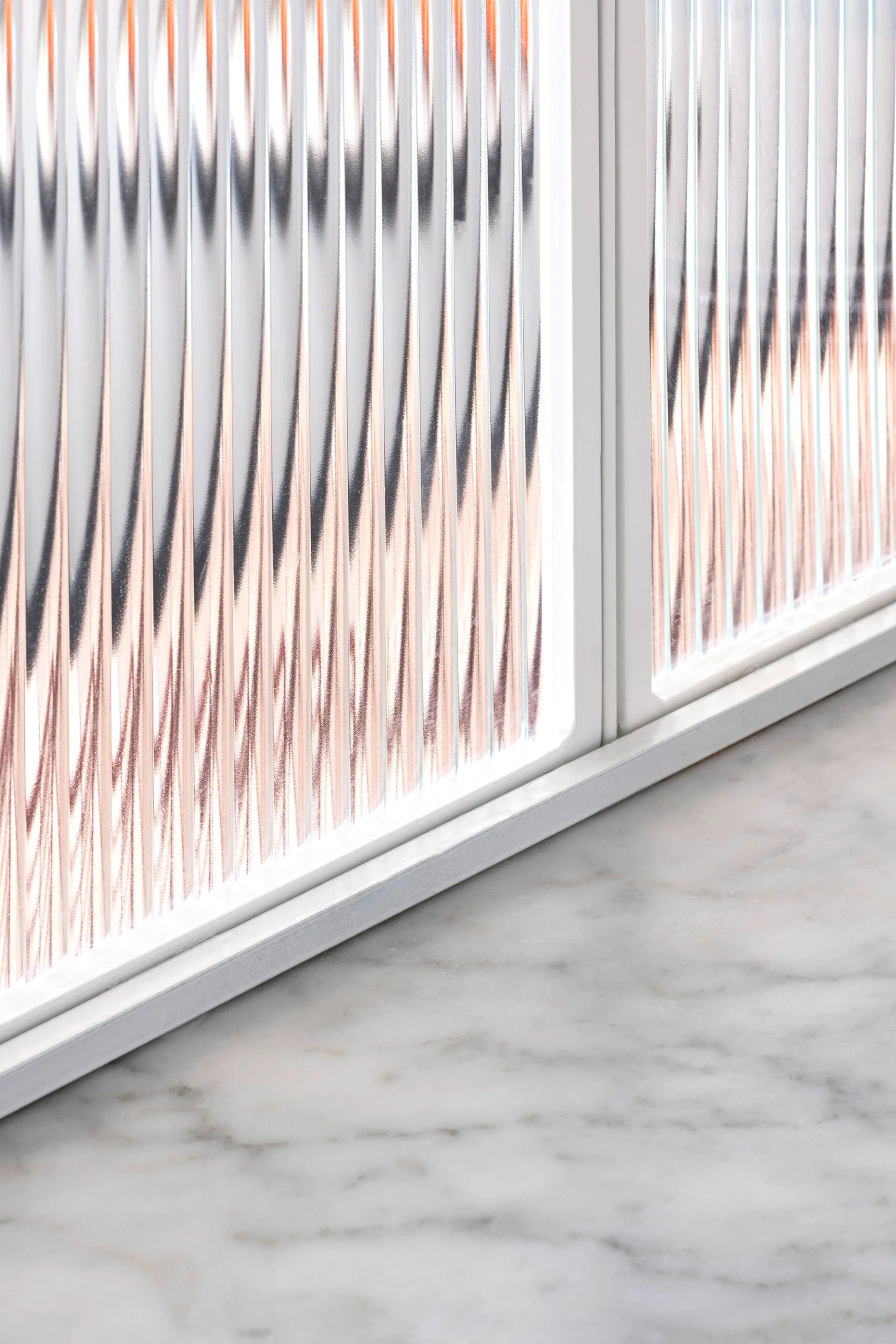 A close-up of a white-framed window with ribbed fluted glass positioned above a polished grey and white veined marble surface.