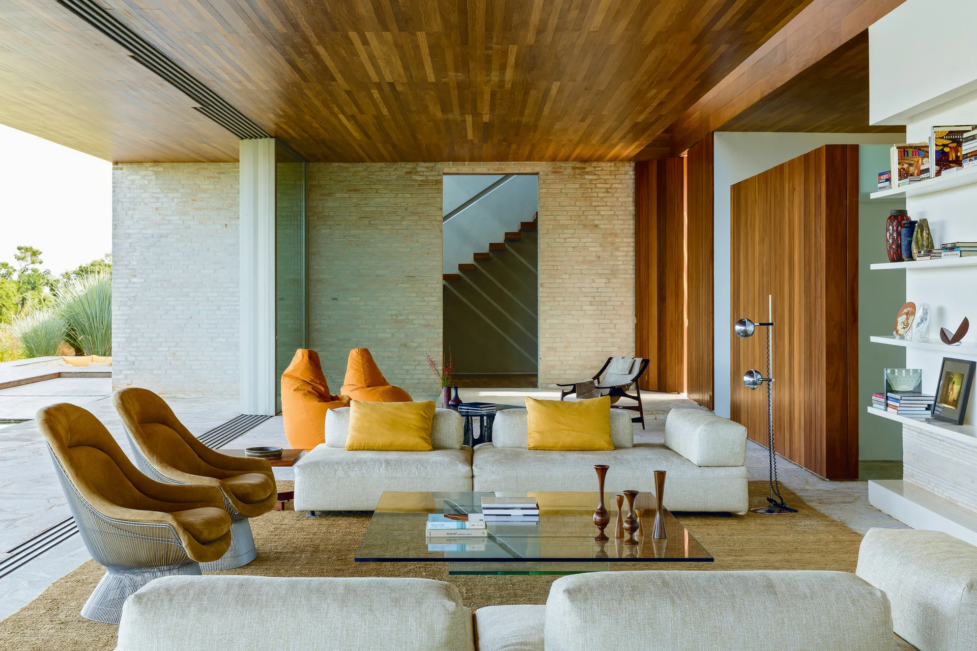 A modern open-plan living room with modular cream sofas, mustard yellow pillows, an exposed brick wall, and a warm wood plank ceiling.