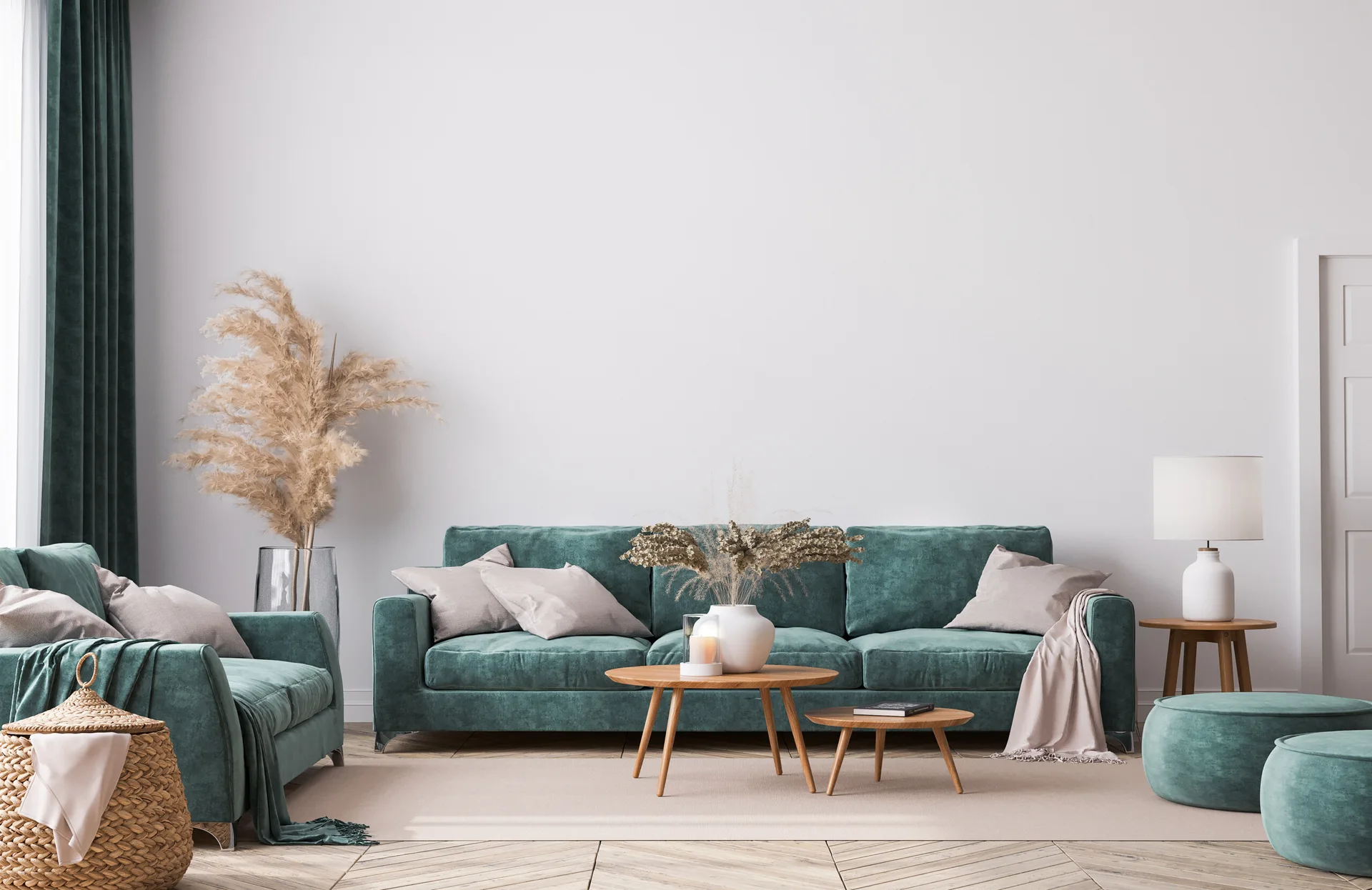 A living room featuring a teal velvet sofa and matching armchair, nested round wooden coffee tables, and herringbone wood flooring under white walls.