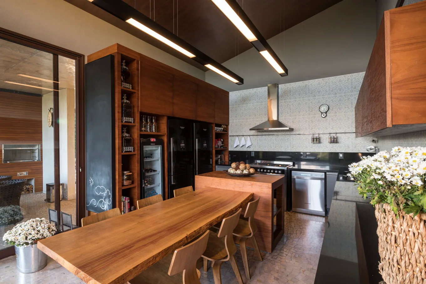 A contemporary kitchen featuring warm wood cabinetry, a live-edge wooden dining table, black appliances, and a blue and white patterned tile wall.