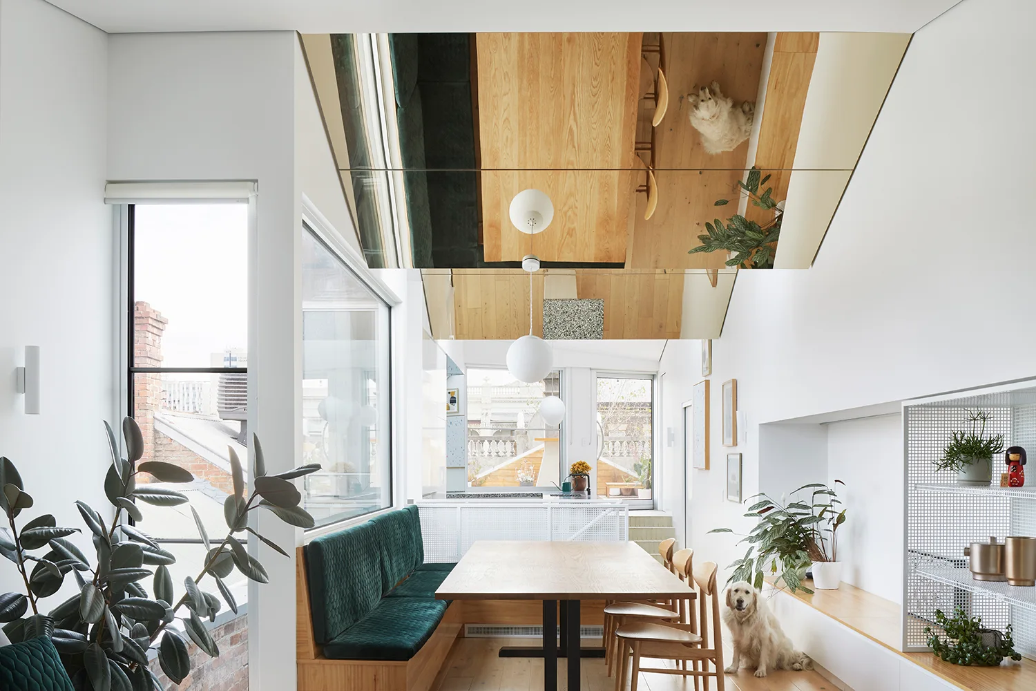A modern dining room features a light wood table, an emerald green velvet banquette, and a striking mirrored ceiling.