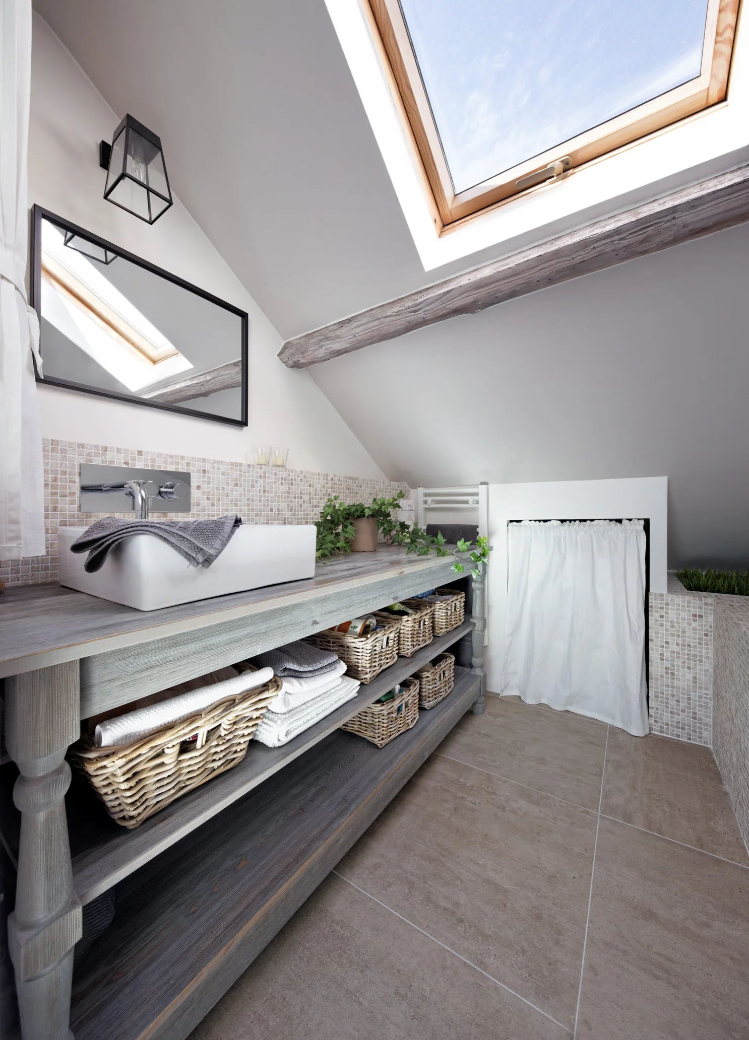 An attic bathroom featuring a gray wooden vanity with woven baskets, a white vessel sink, and a skylight in the sloped ceiling.