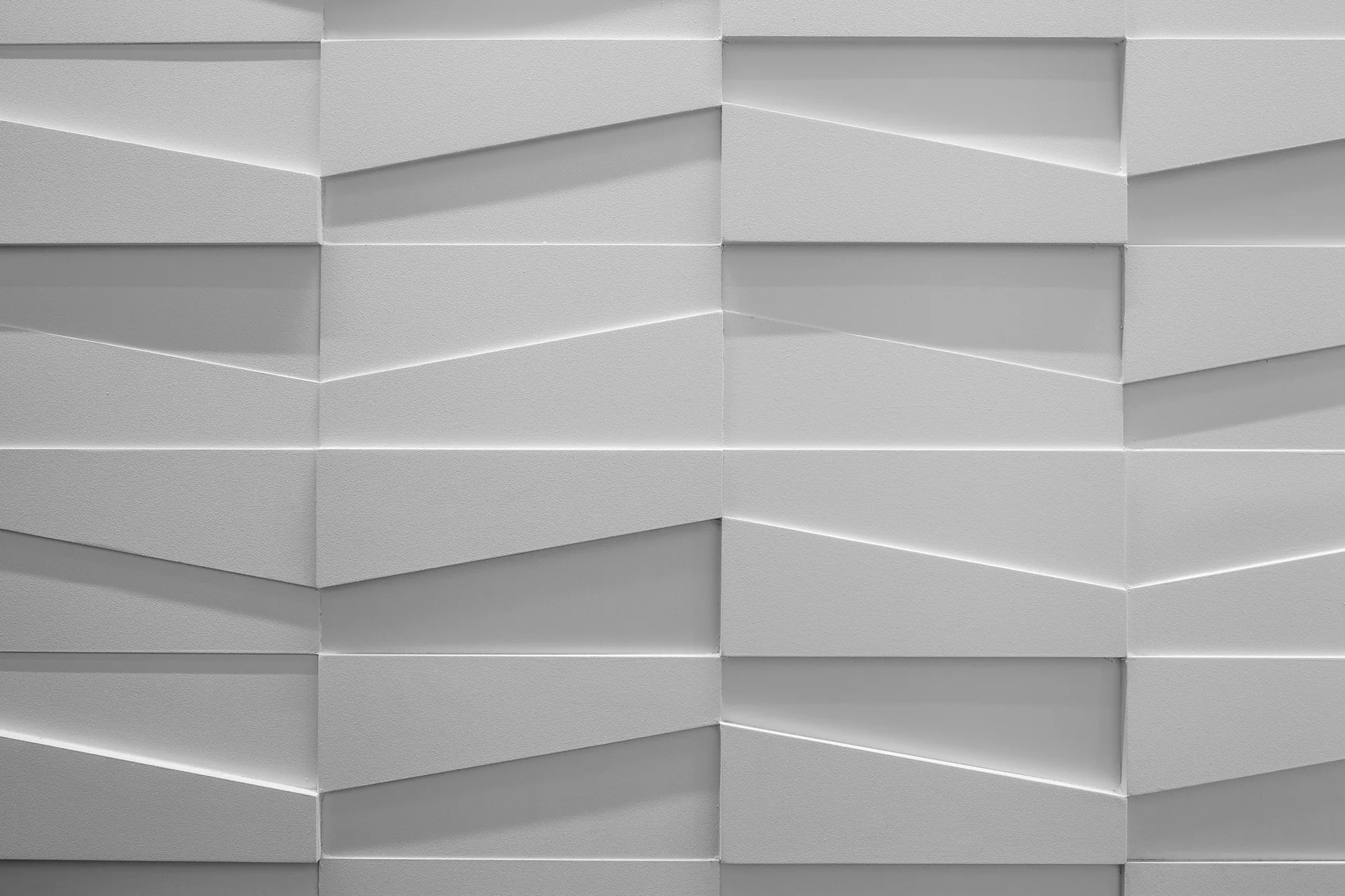 A close-up of white three-dimensional geometric wall panels with an angular matte relief pattern creating subtle shadows.