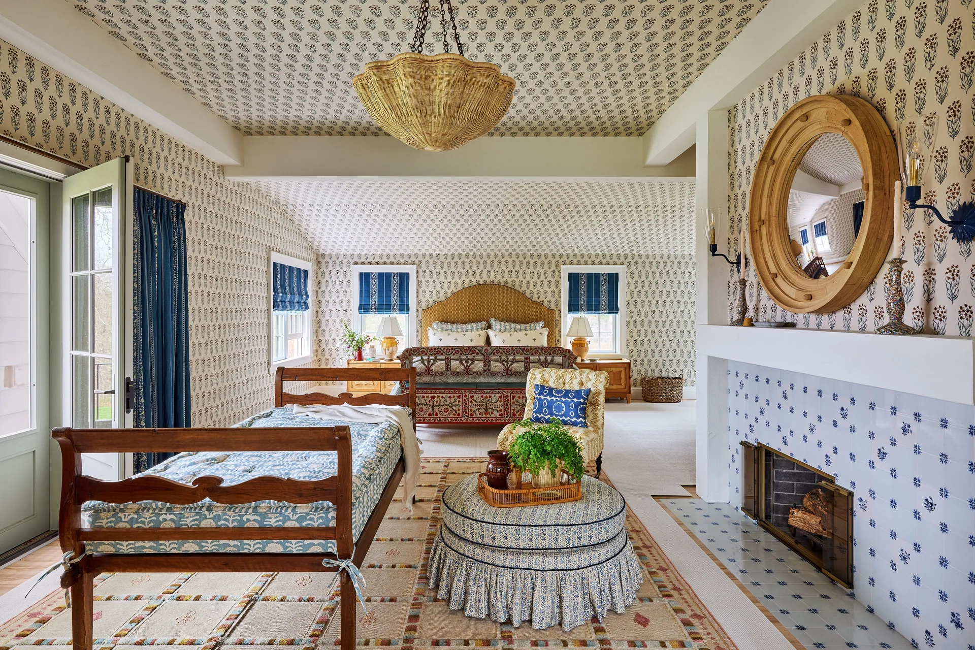 A cottage bedroom features matching floral wallpaper on the walls and ceiling, a tiled blue and white fireplace, and a wood bed.