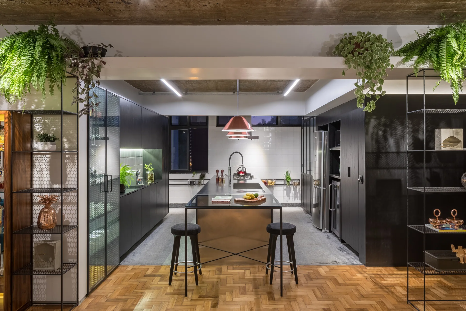 A modern kitchen features matte black cabinetry, a central stainless steel island with bar stools, and a herringbone parquet wood floor.