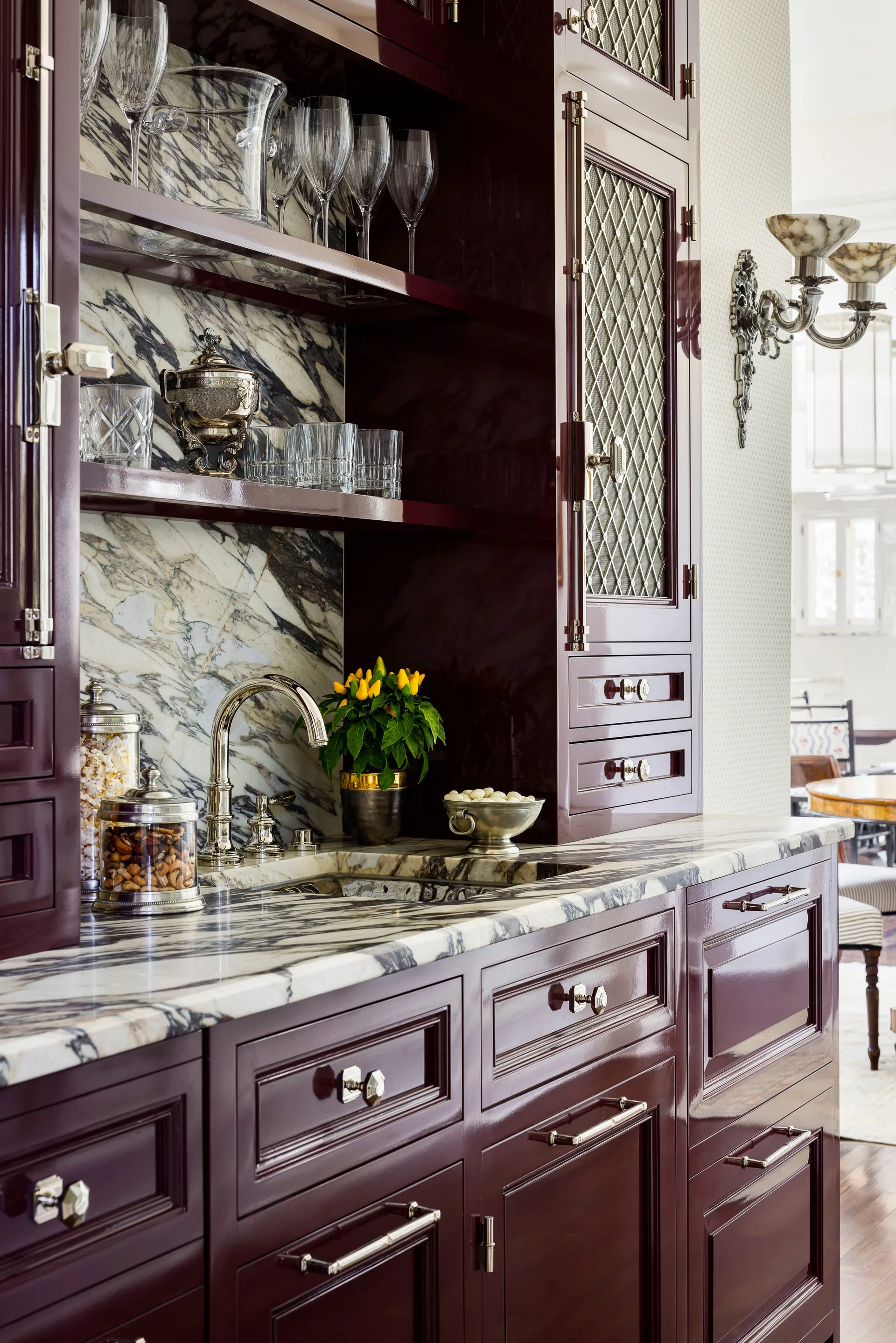 High-gloss plum cabinetry frames a wet bar with a veined marble countertop, matching backsplash, and a polished gooseneck faucet.