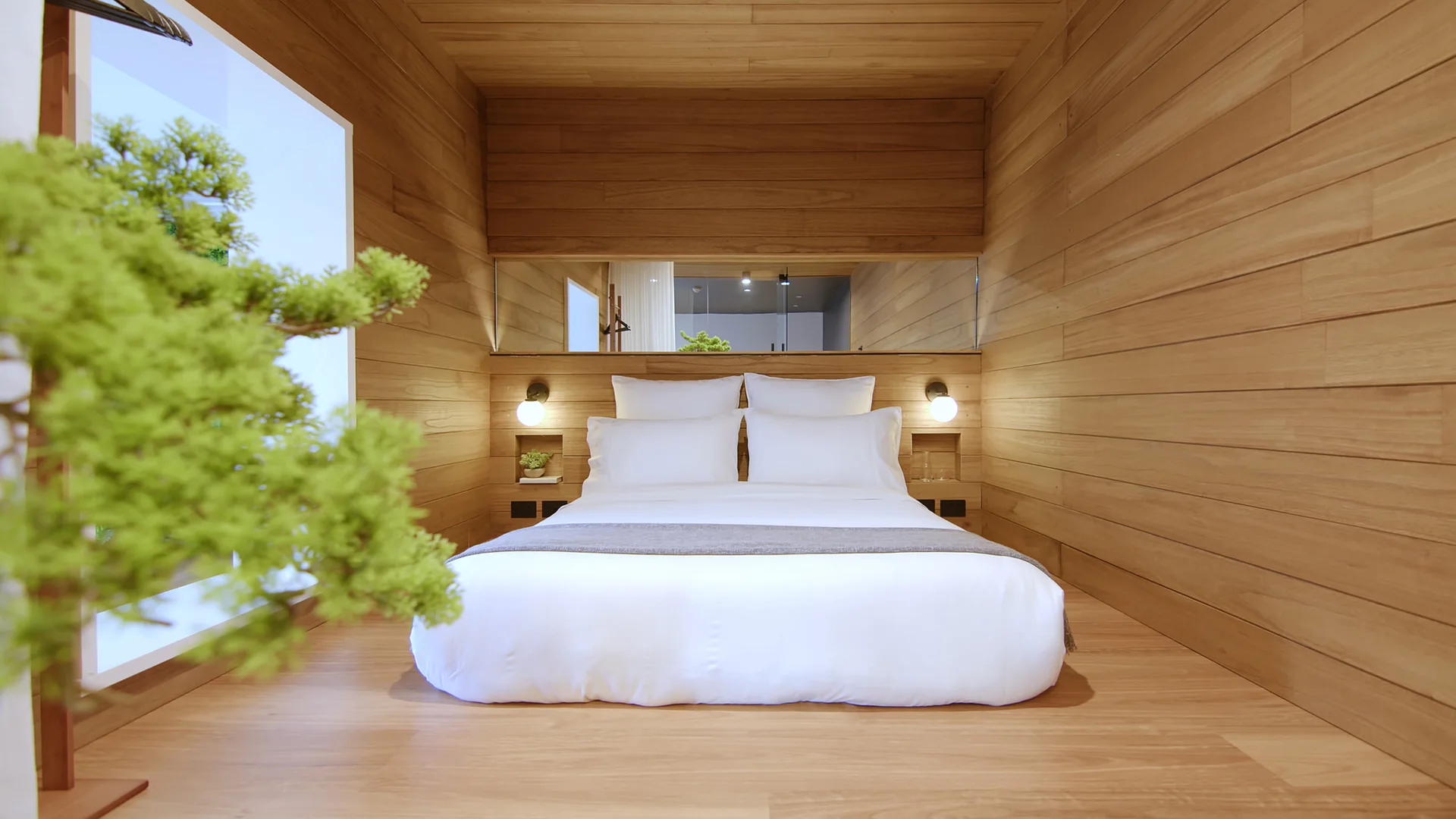 A minimalist bedroom featuring horizontal wood plank walls, a white bed with built-in niches, and a slim horizontal mirror above the headboard.