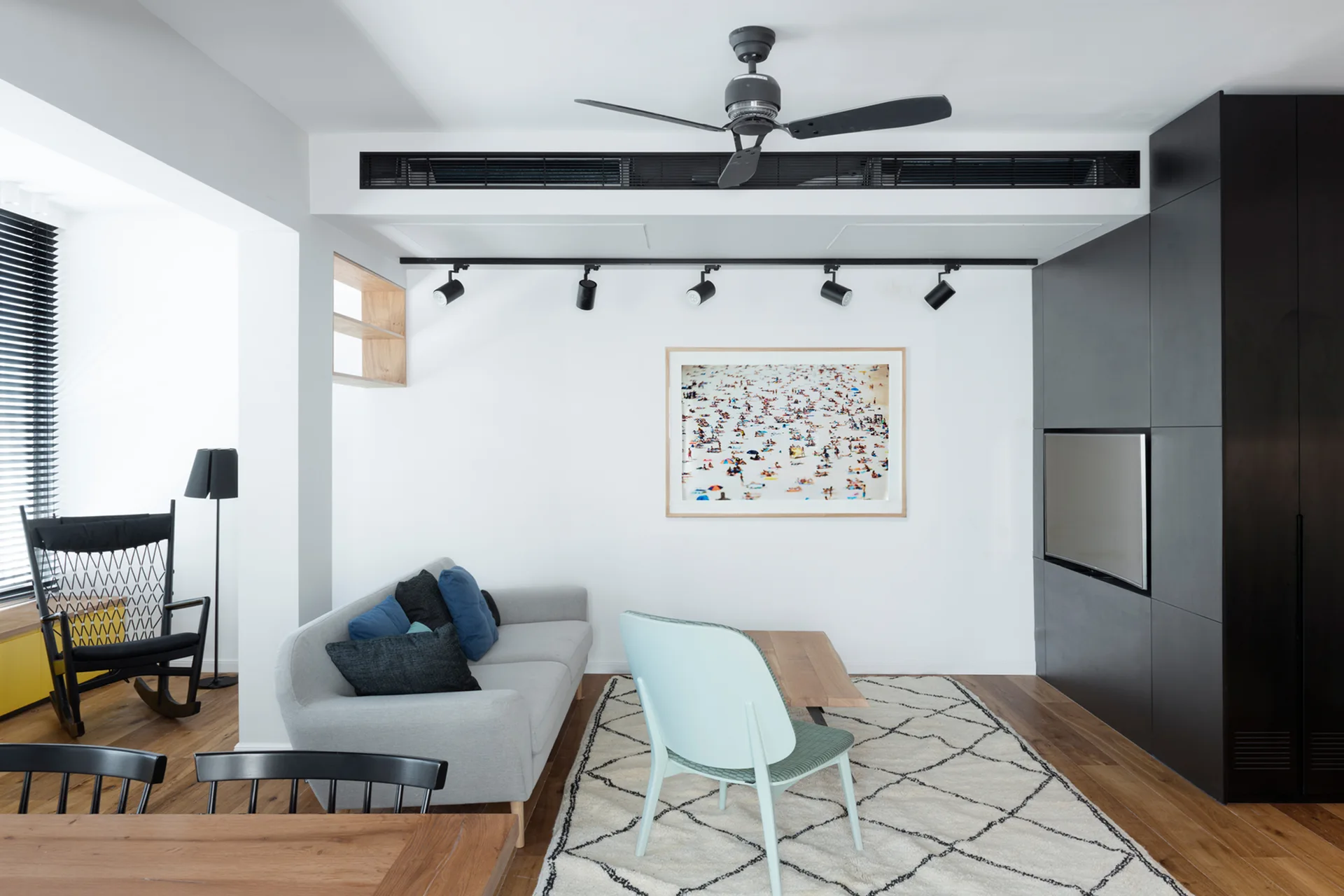 A contemporary living room featuring a grey sofa, a light blue chair, a patterned area rug, and a large matte black built-in storage wall.