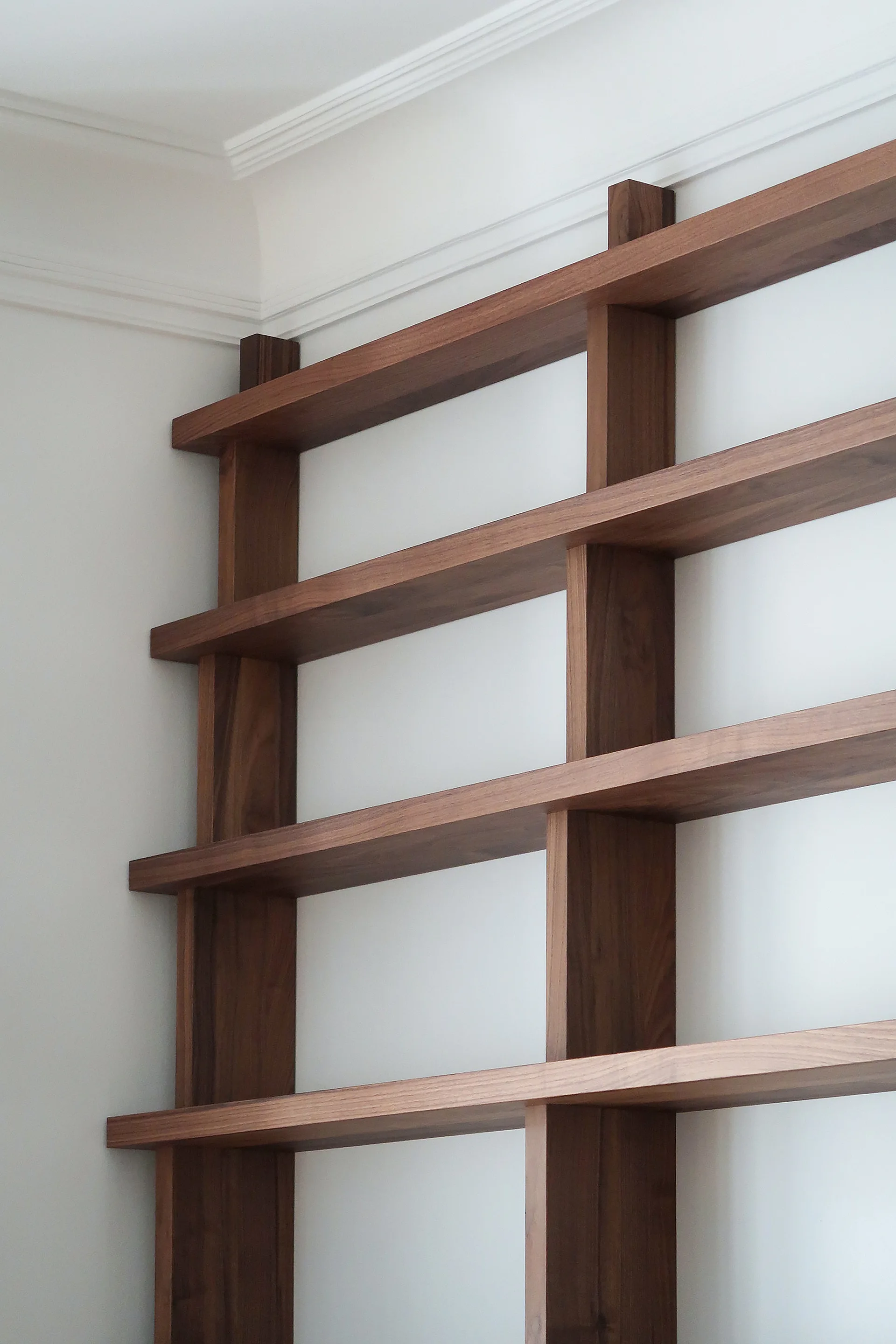 A minimalist warm wood open shelving unit mounted against a plain white wall beneath white crown molding.