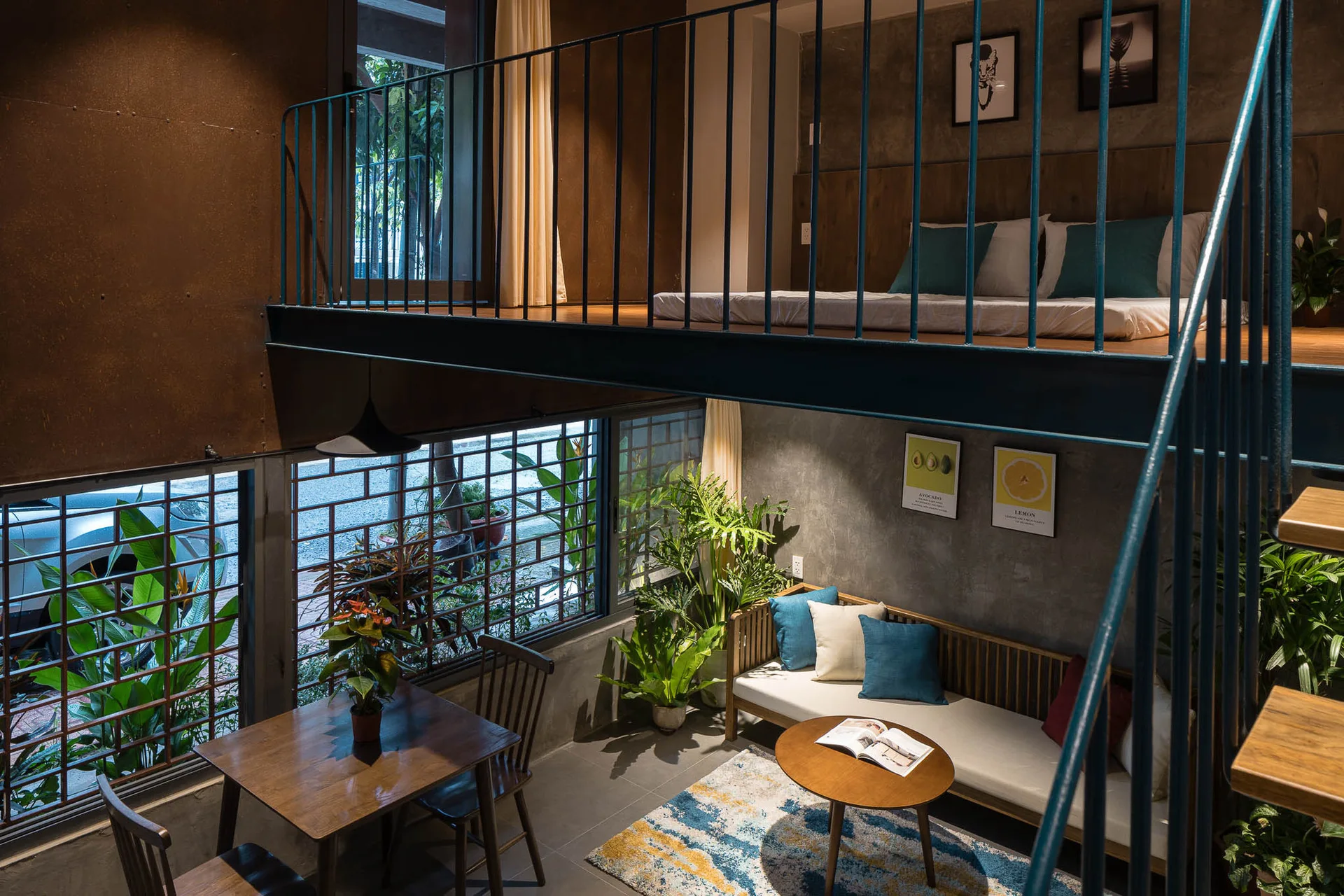 A split-level industrial loft featuring a lower living area with a wooden sofa and a dining table beneath a mezzanine bedroom with a metal railing.
