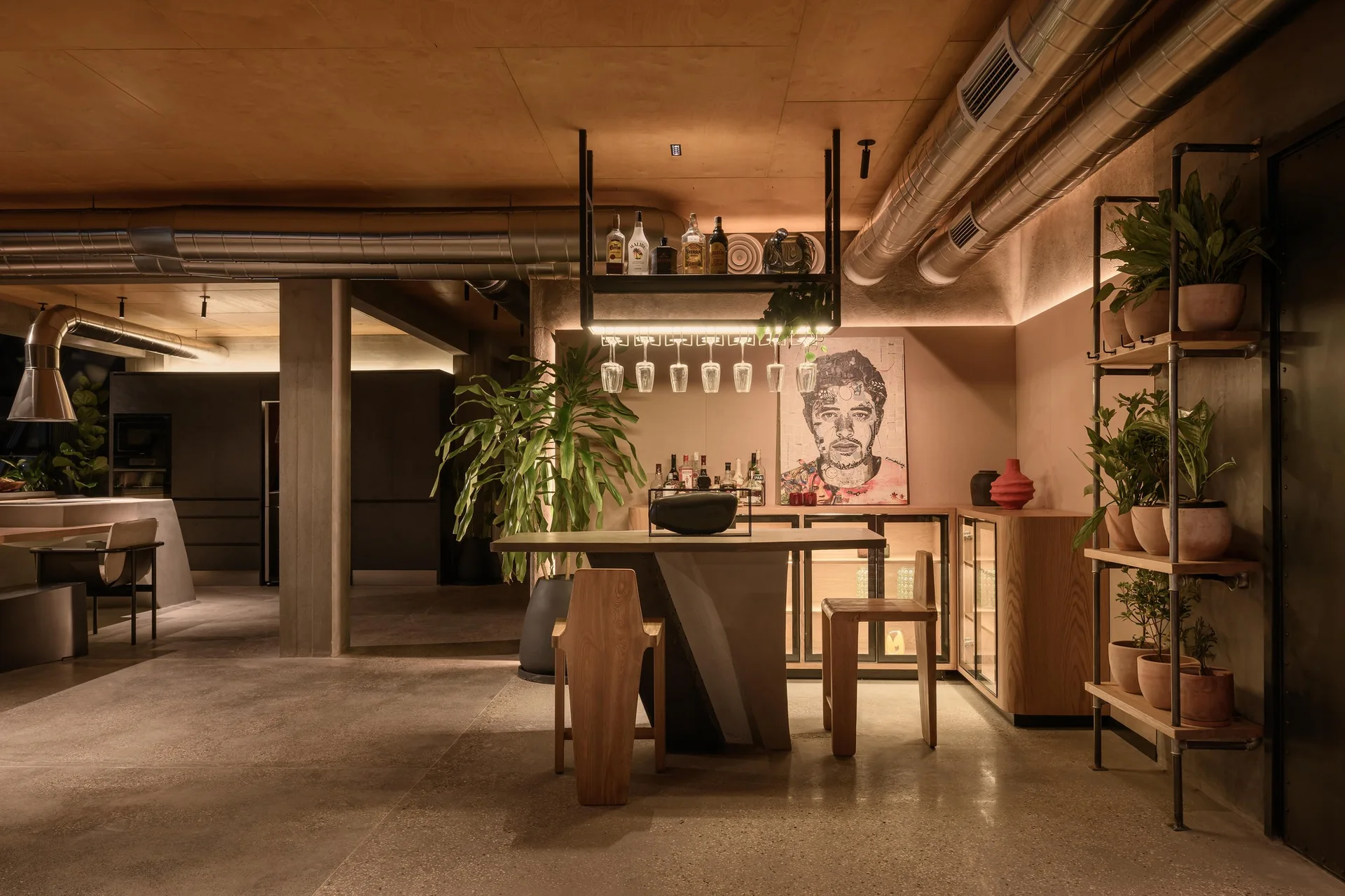 A modern industrial home bar features a concrete and wood counter with wooden stools, exposed metal ceiling ducts, and warm ambient lighting.