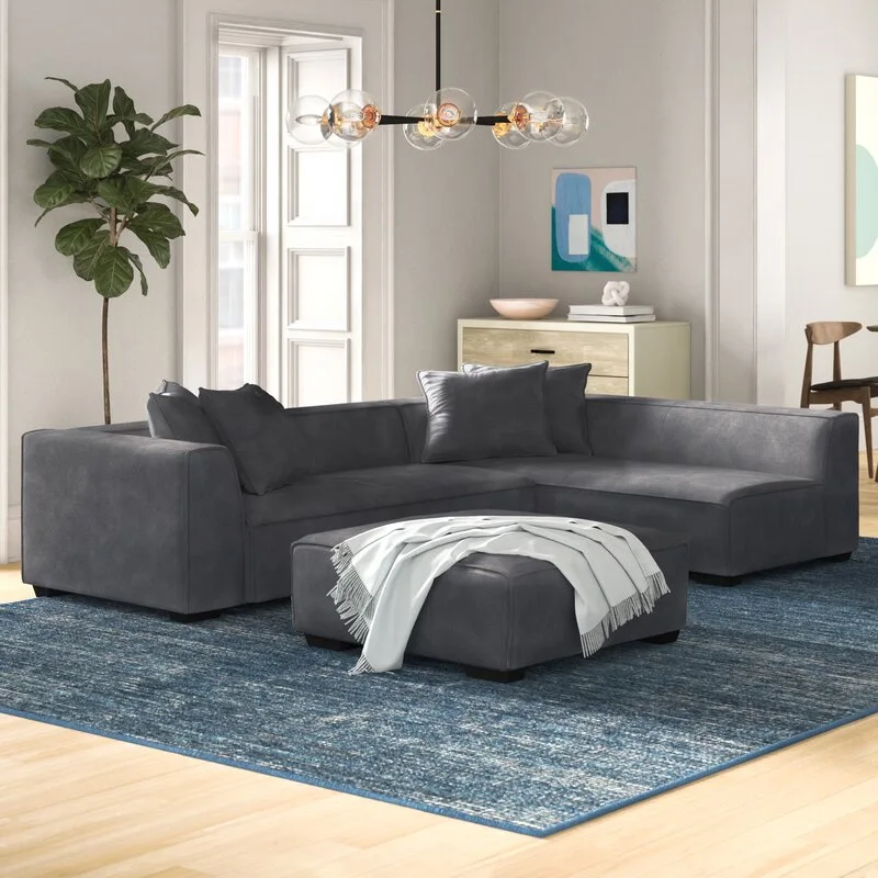 A modern living room features a large charcoal grey sectional sofa and matching ottoman arranged on a blue textured rug under a globe chandelier.