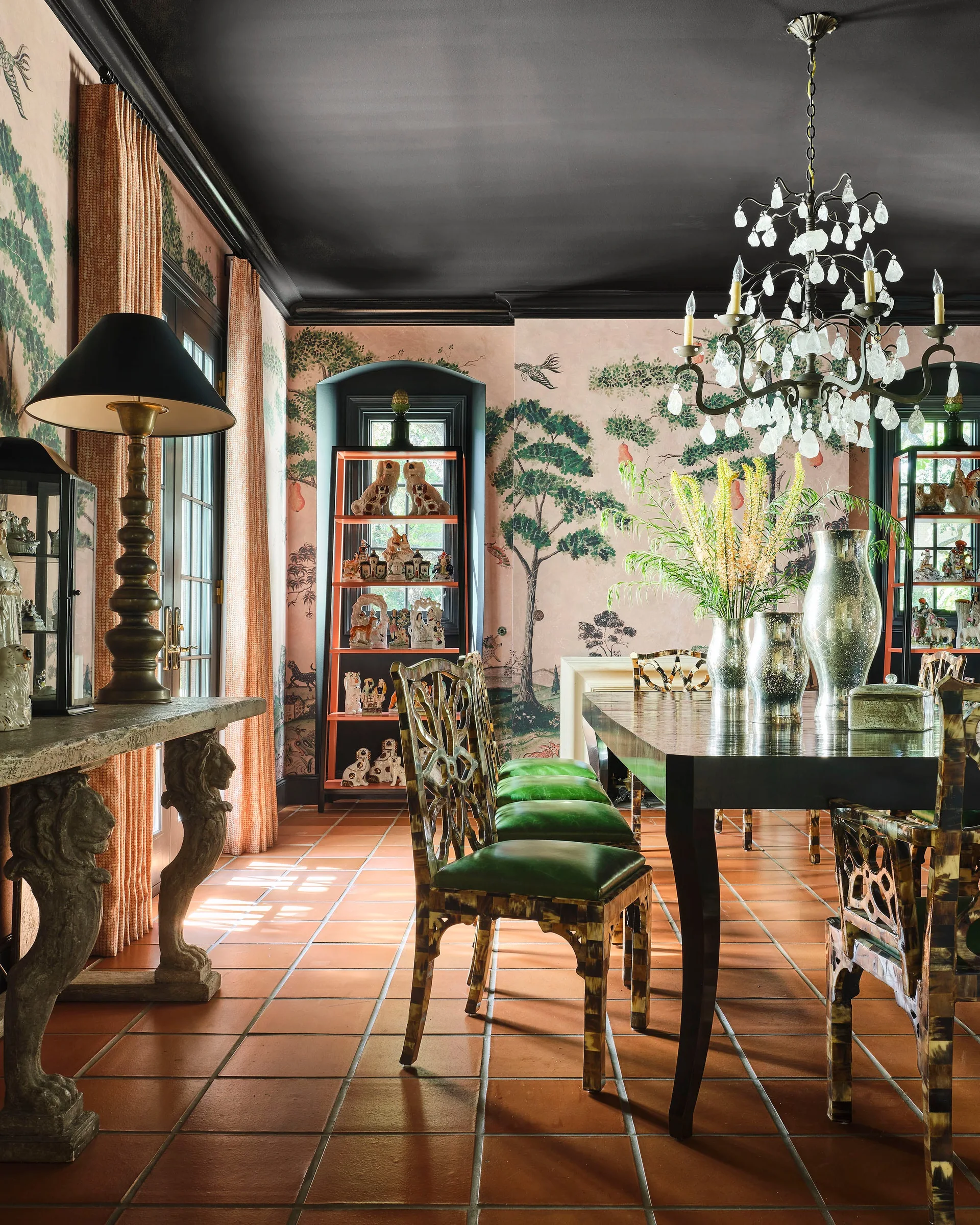 A formal dining room featuring pink chinoiserie wallpaper, terracotta tile flooring, a black painted ceiling, and green upholstered chairs.