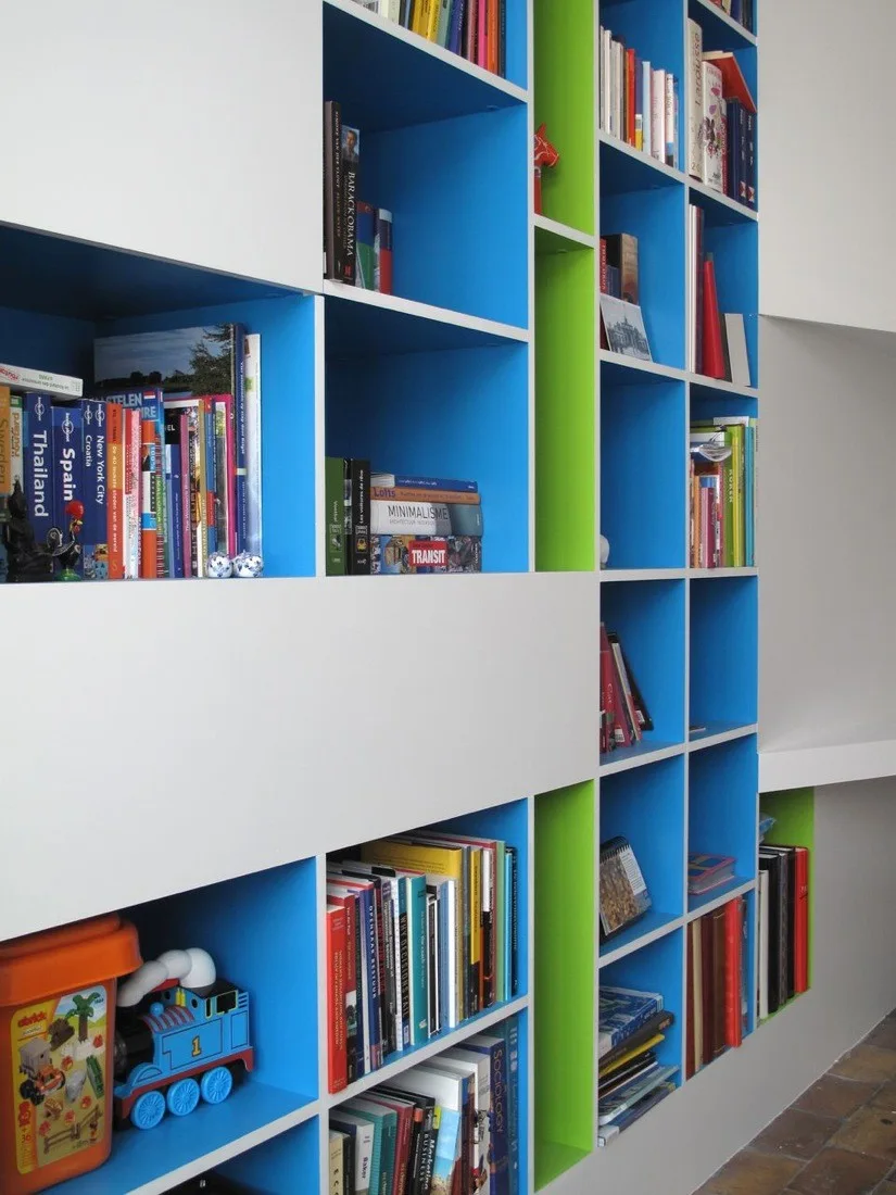 A built-in white shelving unit features a grid of blue and green painted compartments filled with books and a toy train.