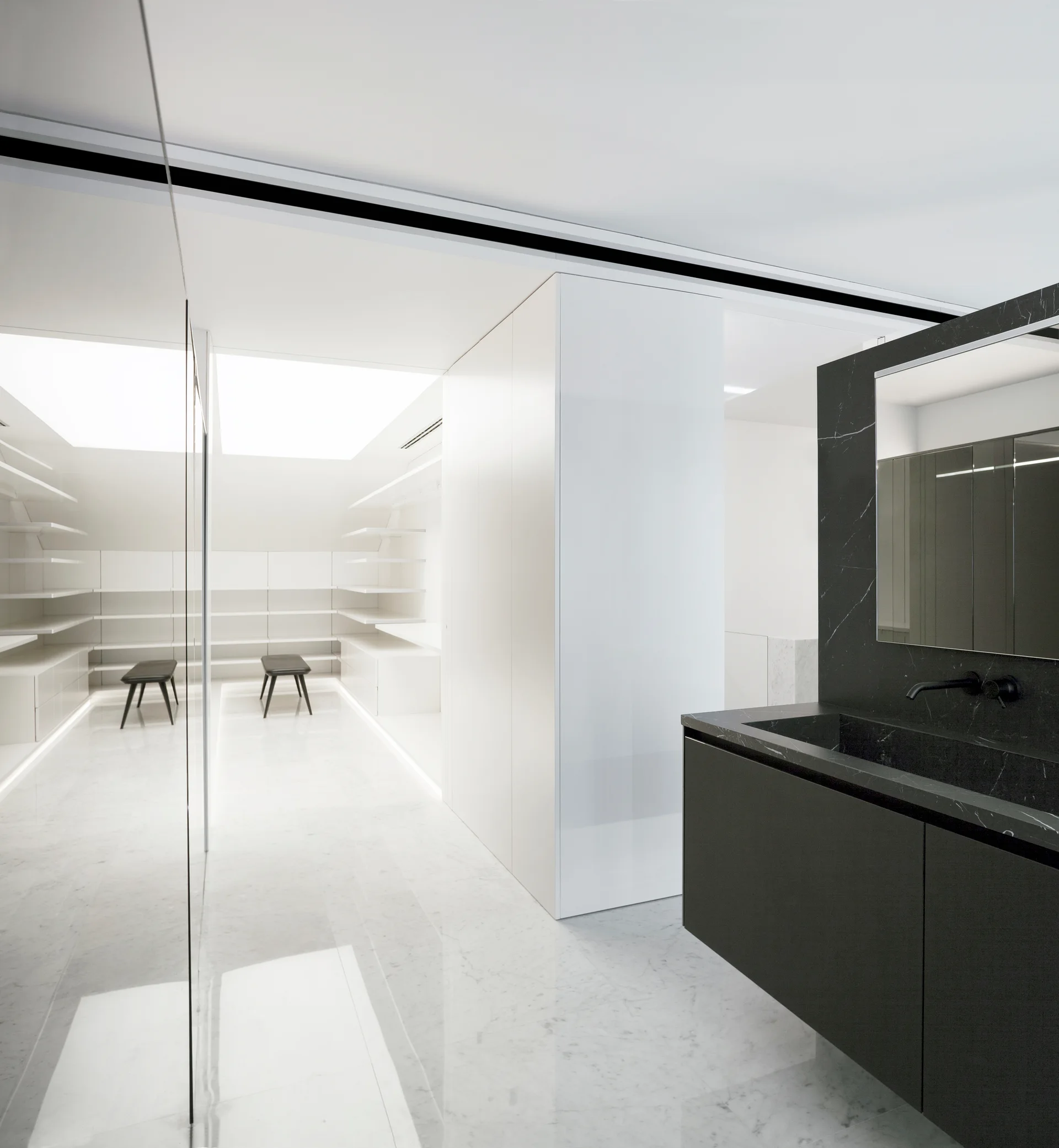 A modern bathroom features a dark stone vanity and a bright white walk-in closet with marble floors and open shelves.