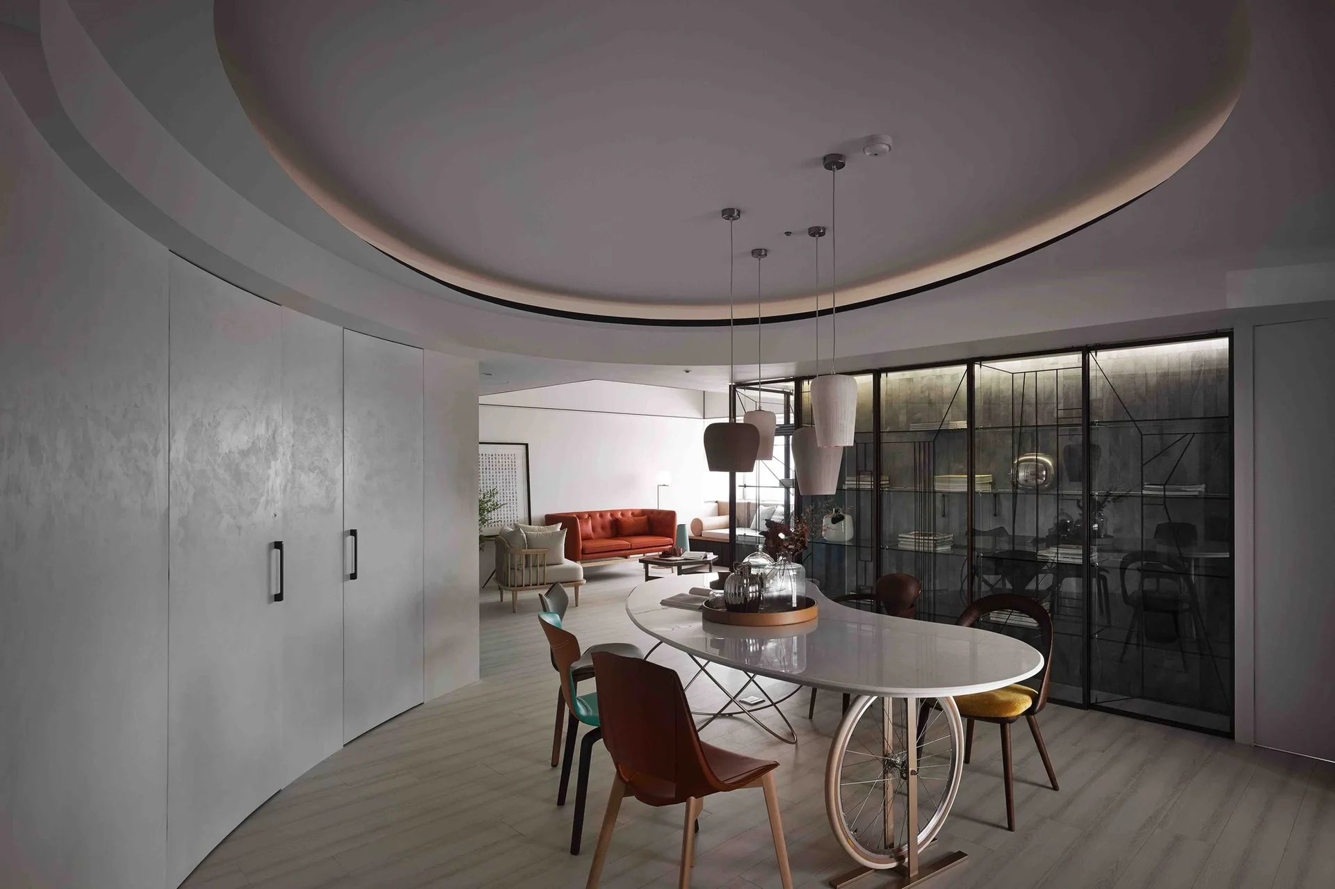 An eclectic dining room features a curved white table with a bicycle wheel base, modern dining chairs, and a large circular recessed ceiling.