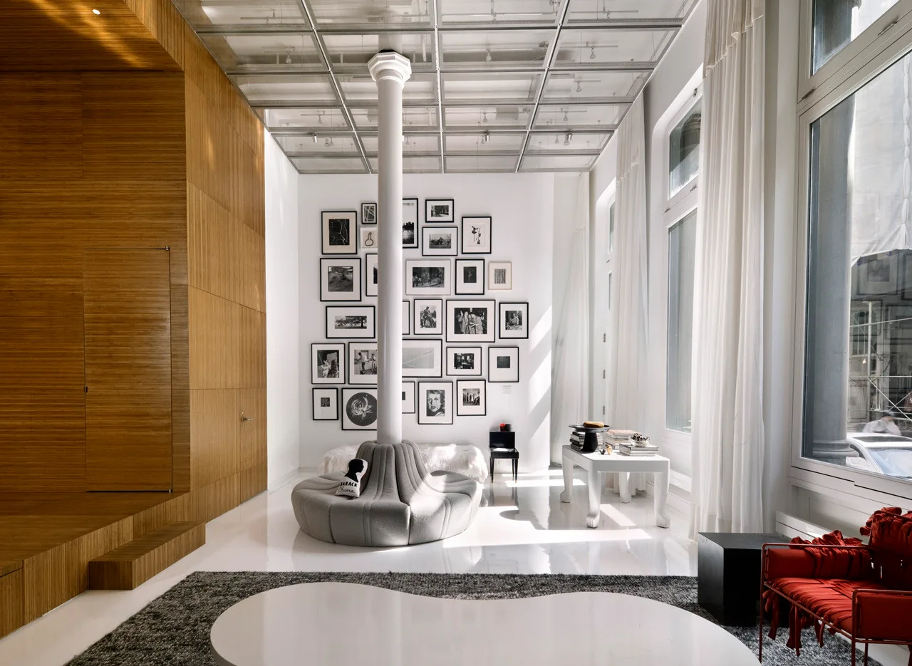 A loft living room features a grey circular sofa built around a white column, backed by a gallery wall and a warm wood-paneled wall.