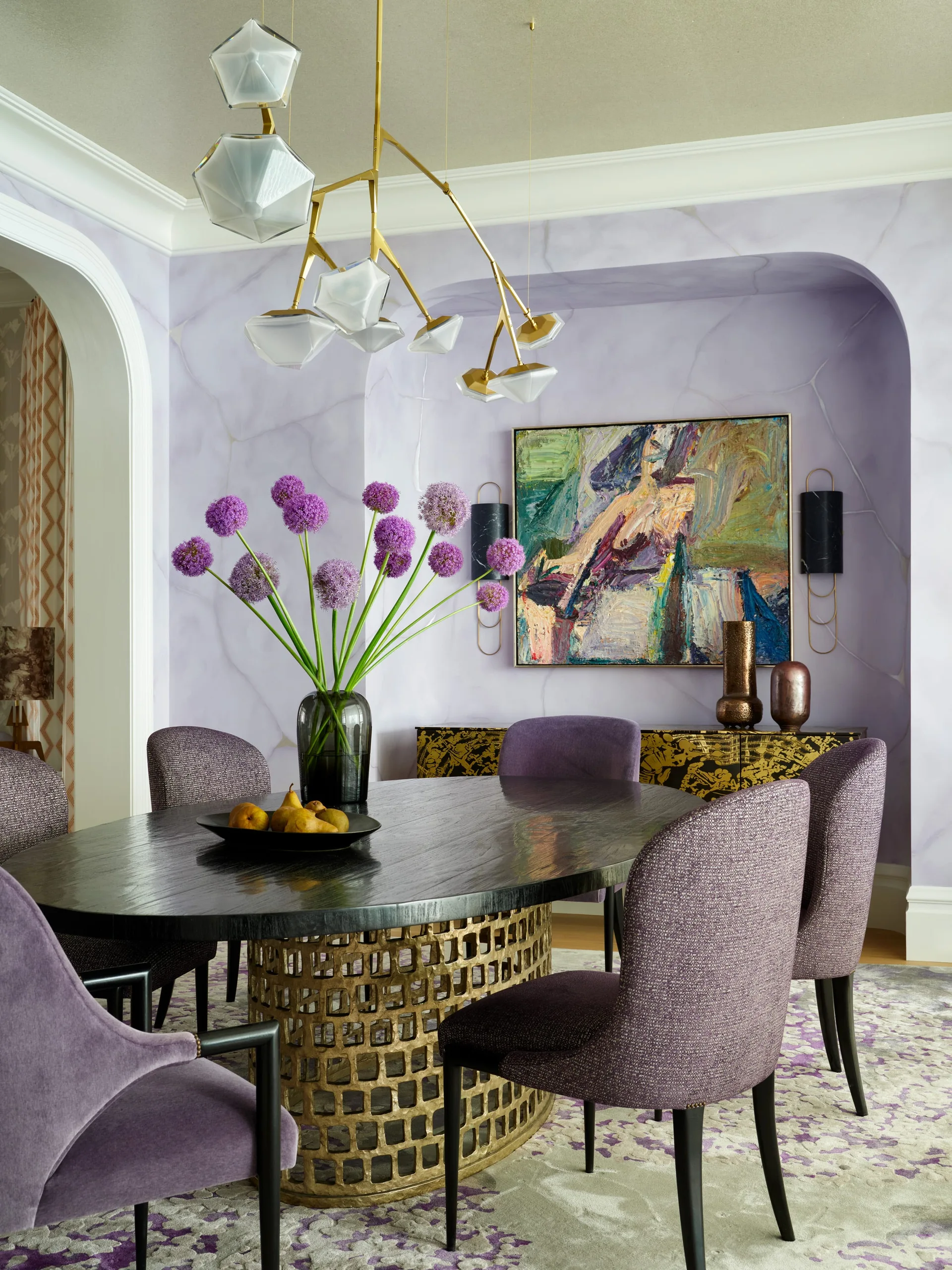 A dining room features purple upholstered chairs around a black oval table with a gold lattice base, set against a marbled lavender arched alcove.