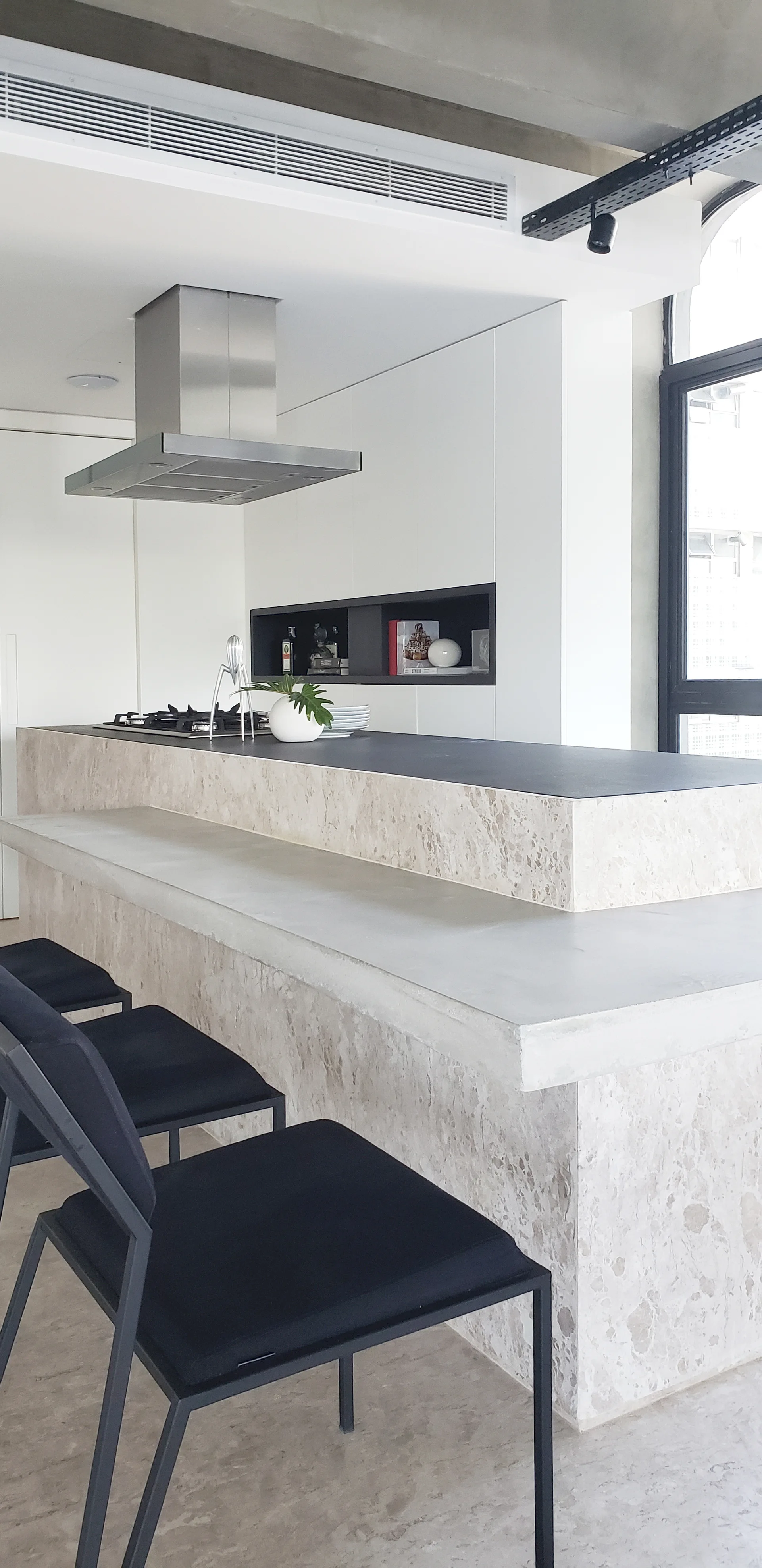 A modern kitchen featuring a double-tiered stone island with a black countertop, black bar stools, and white minimalist cabinets with a recessed shelf.