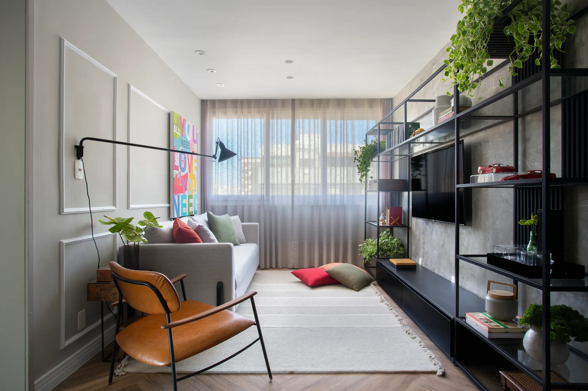 A contemporary living room features a grey sofa, a tan leather armchair, and a tall black metal shelving unit against a textured grey wall.