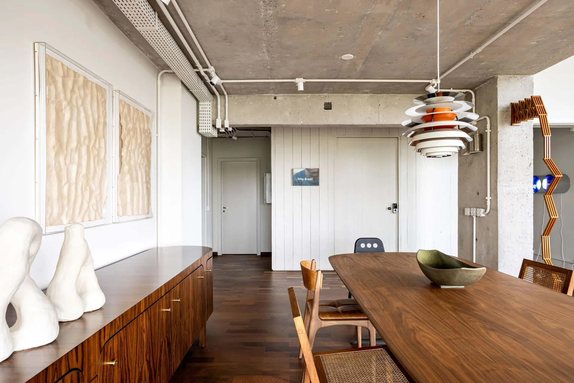A modern dining room features a dark wood dining table, matching sideboard, cane-back chairs, and an exposed raw concrete ceiling.