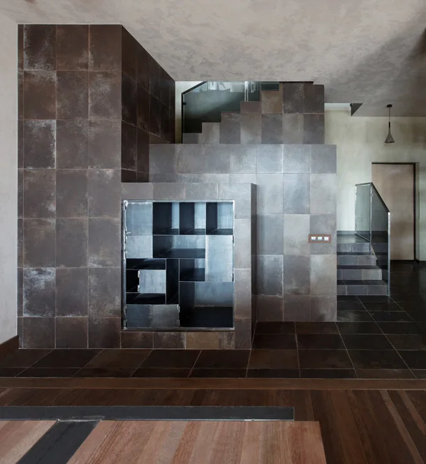 A minimalist staircase clad in dark brown square tiles features a recessed black metal grid shelving unit and glass railings.