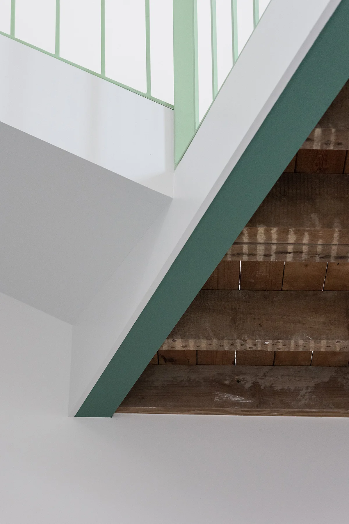An architectural close-up of a white staircase featuring natural wood treads and a painted sage green metal railing.