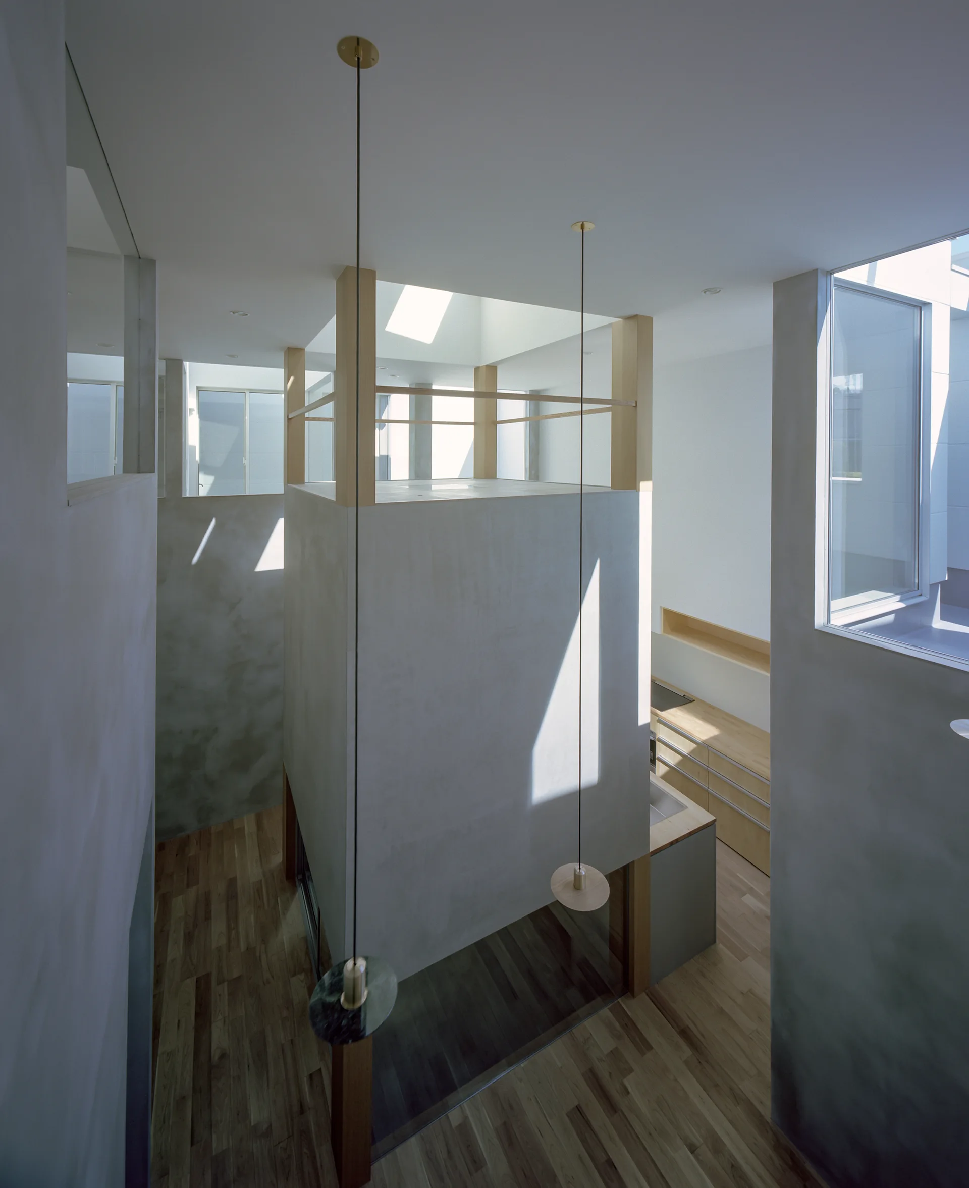 Looking down into a minimalist multi-level home featuring a central grey plaster volume, light wood flooring, kitchen cabinets, and skylights.