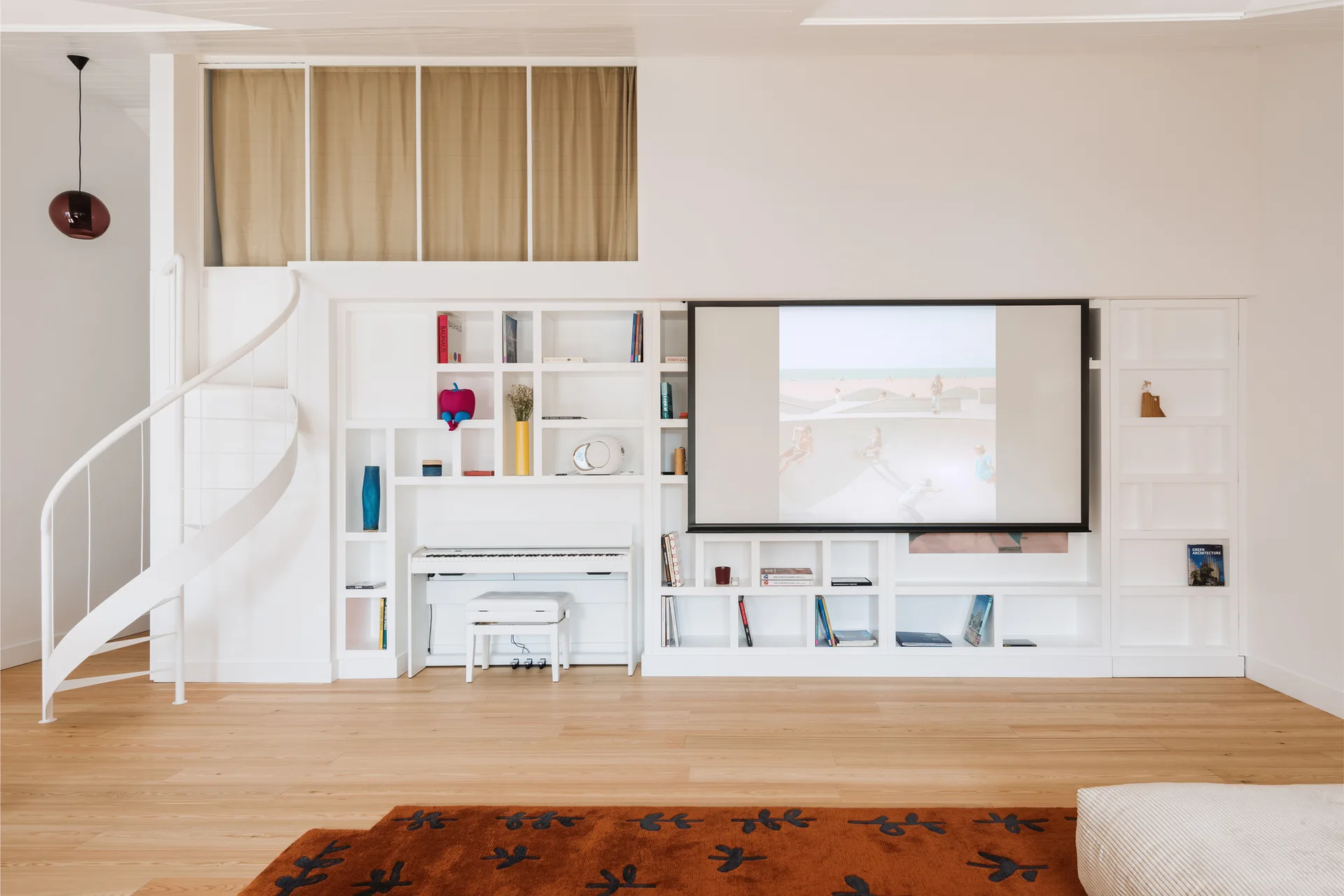 A bright living room featuring a custom white built-in bookcase with an integrated piano, a projection screen, and a white spiral staircase on the left.