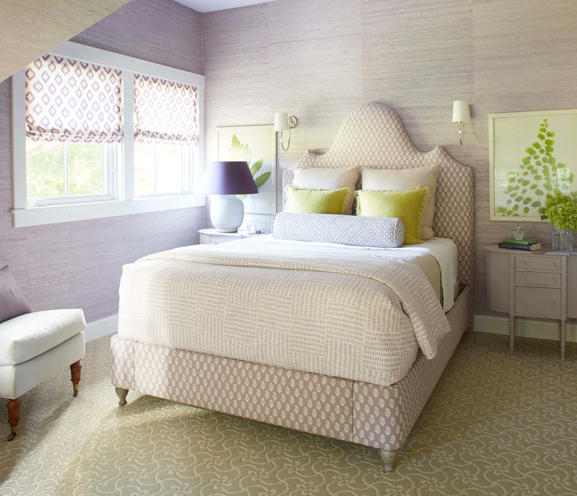 A lavender bedroom featuring a patterned upholstered headboard, textured grasscloth wallpaper, and matching bedside tables with lamps.