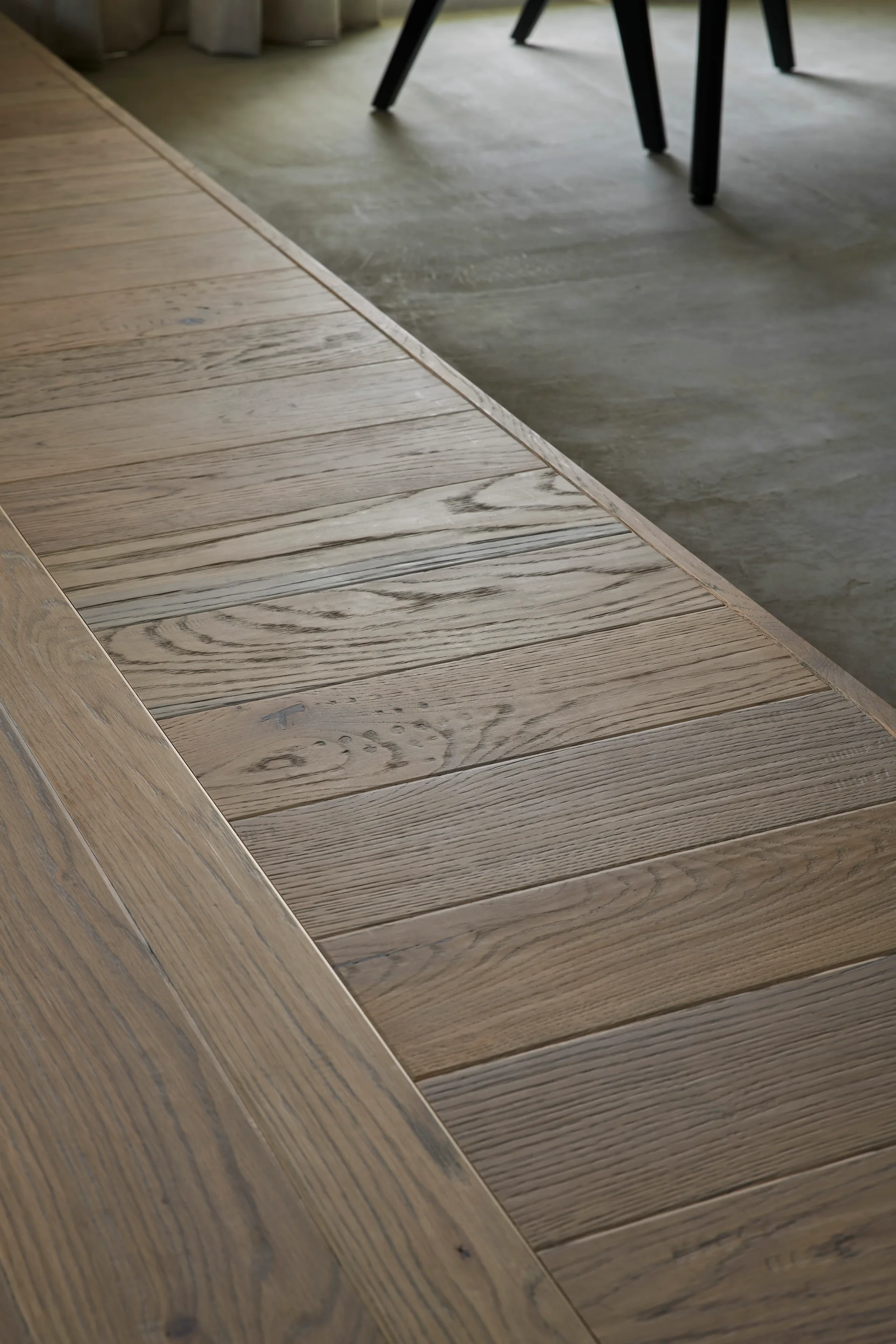 A close-up view shows a flush floor transition where light brown wooden planks meet a smooth grey concrete surface.