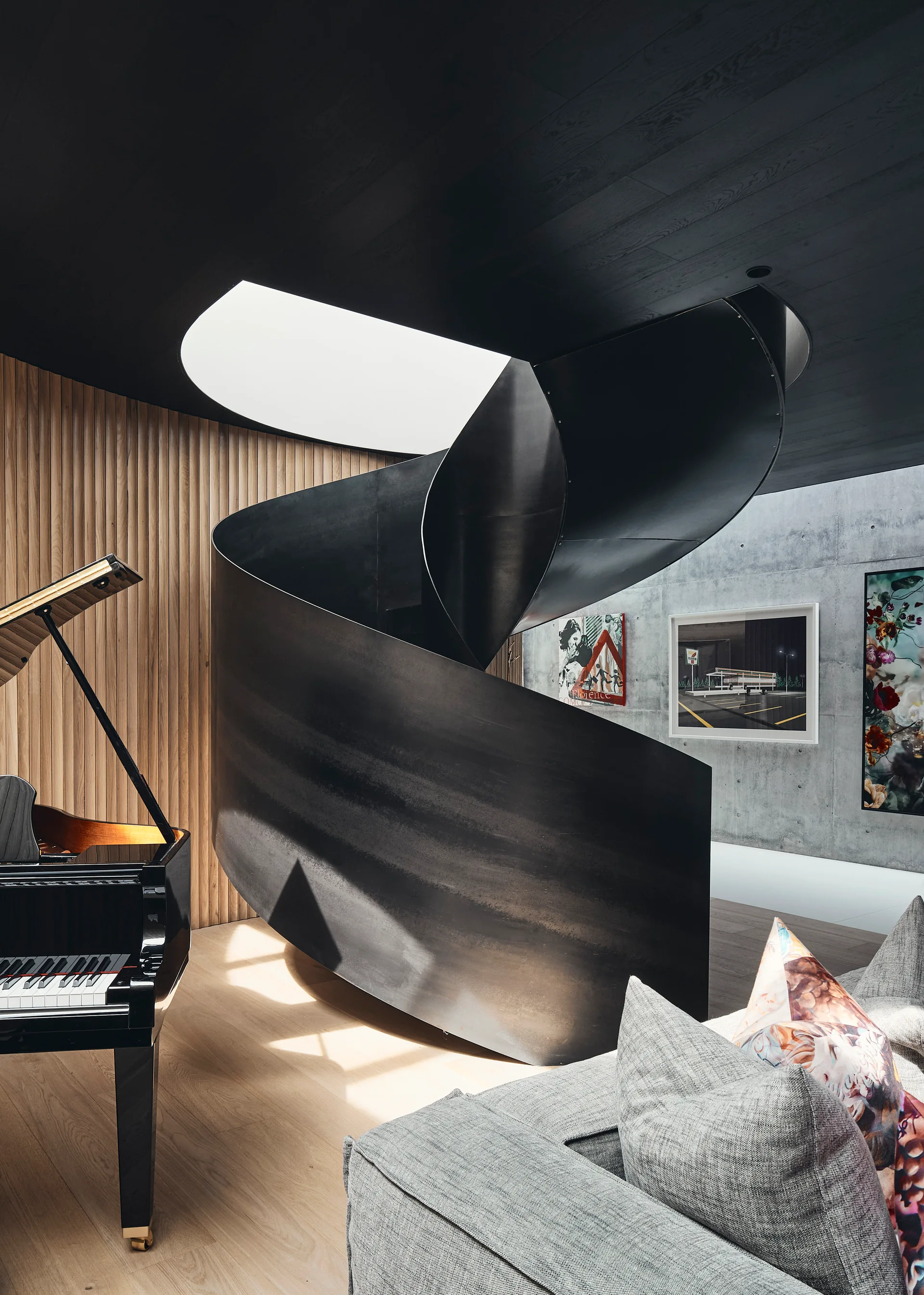 A modern living room features a dramatic black metal spiral staircase beneath a circular skylight, alongside a grand piano and wood-slatted wall.