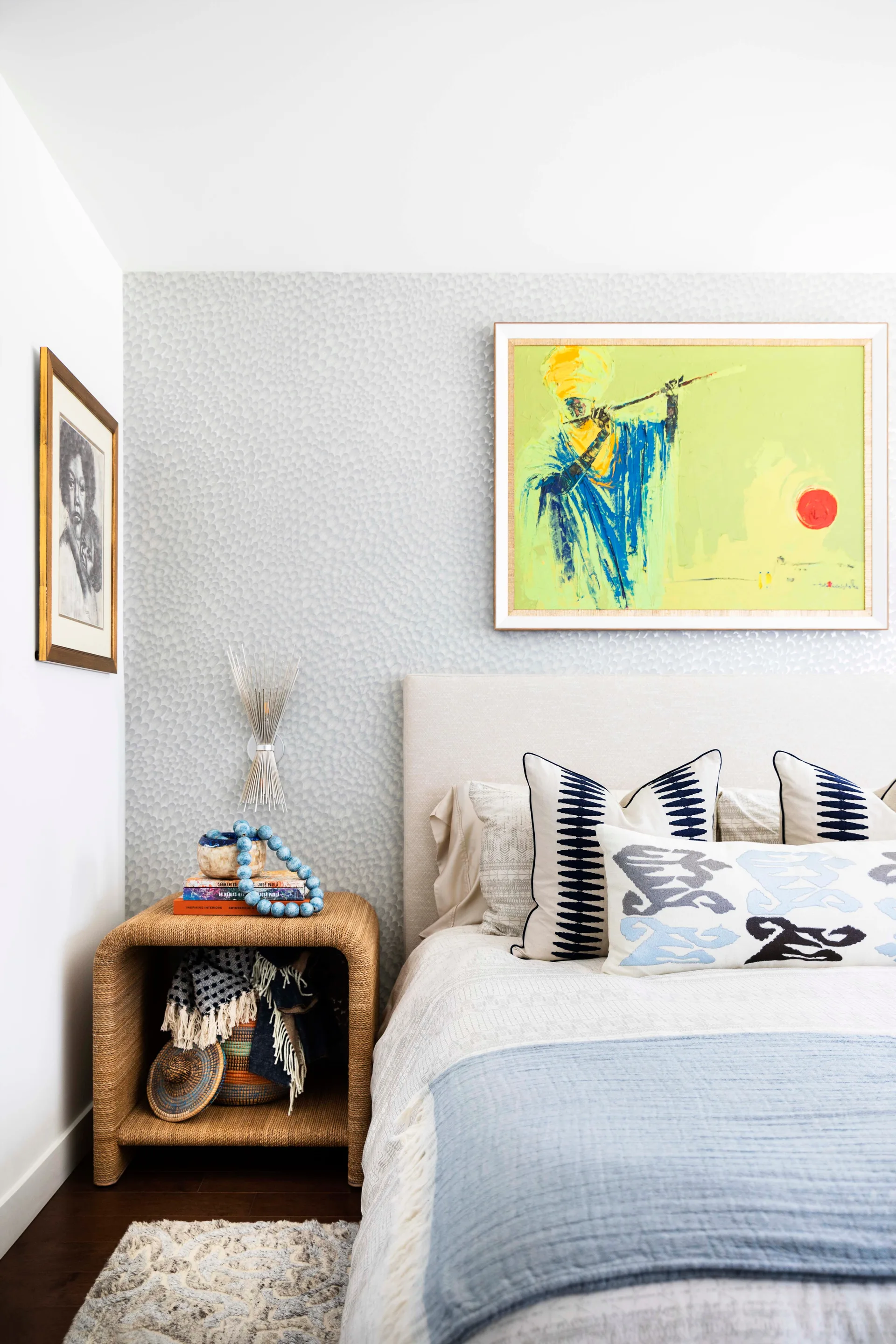 A bedroom corner features an upholstered beige headboard and a woven rattan nightstand against a grey textured wallpaper background.