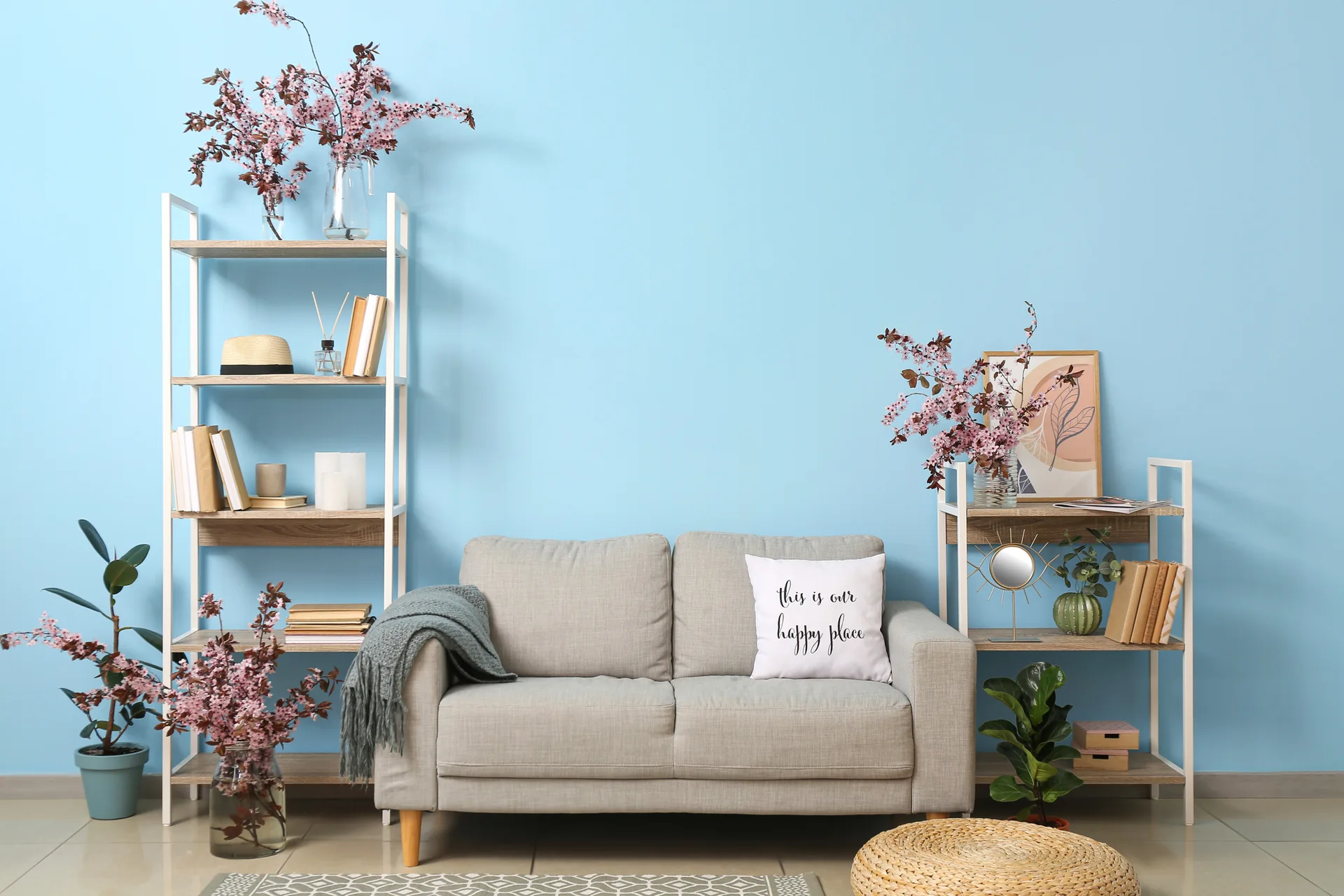 A light grey sofa sits against a sky blue wall between two symmetrical open wood bookshelves decorated with pink blossom branches and books.