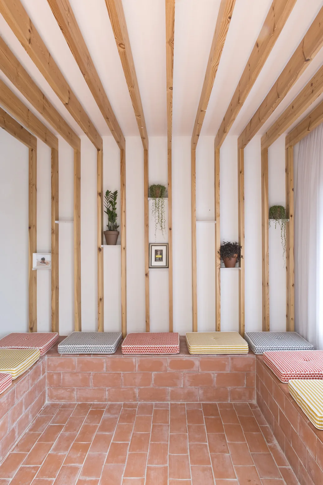A built-in terracotta brick bench with colorful geometric cushions sits in a room with vertical wood slats on the walls and ceiling.