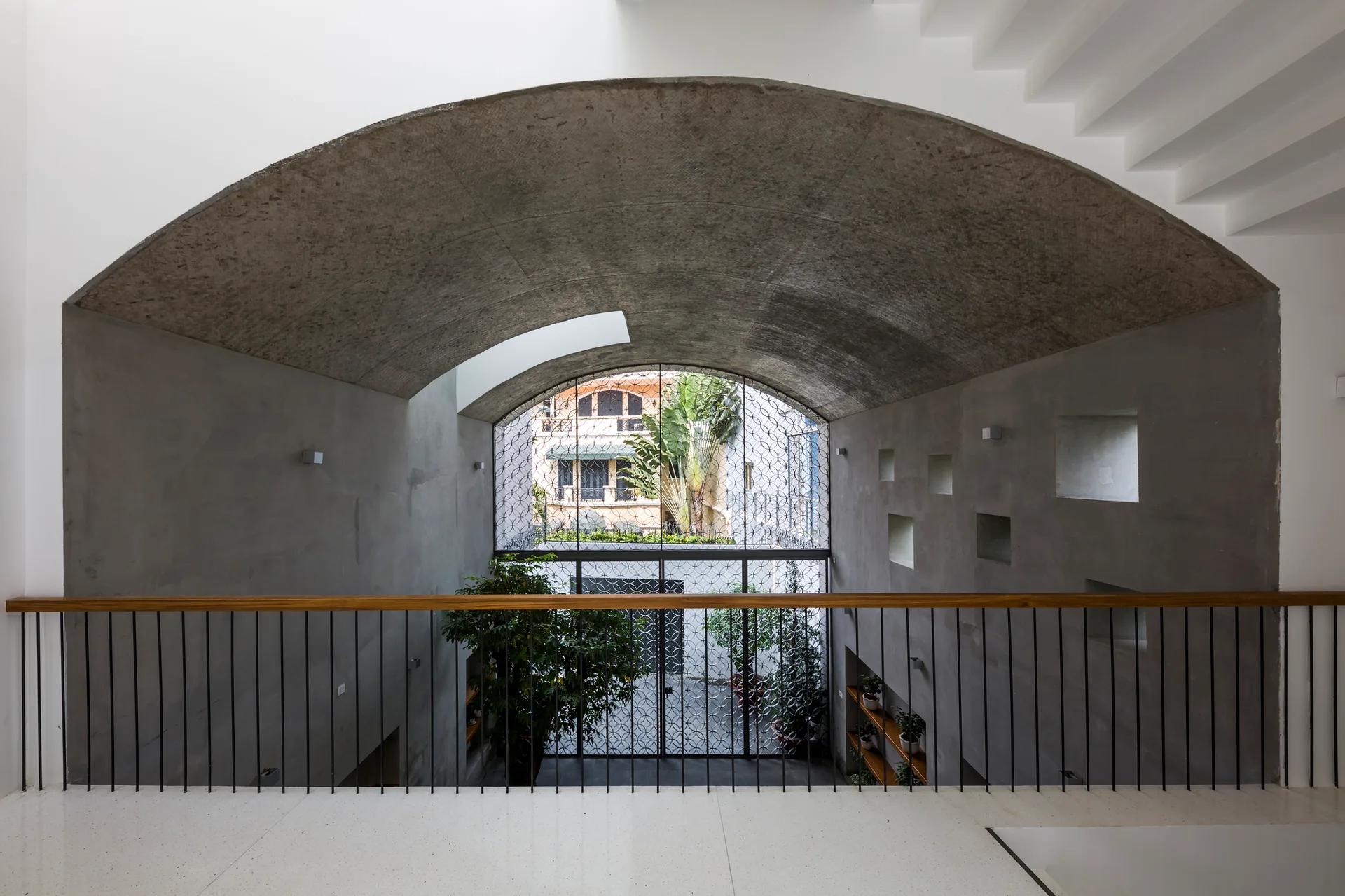 An elevated indoor landing features a white terrazzo floor, black metal railing, and raw concrete walls under an arched barrel vault ceiling.