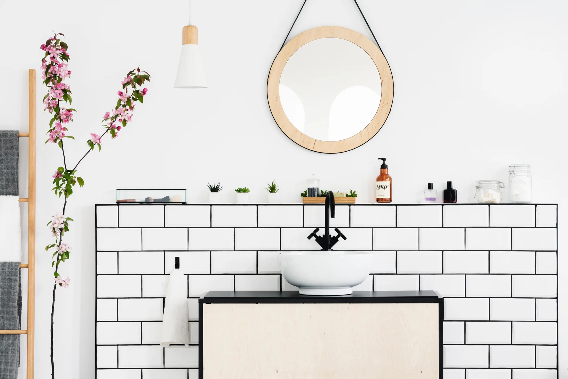A minimalist bathroom features a light wood vanity, a white vessel sink, a black faucet, and a white subway tile backsplash with dark grout.