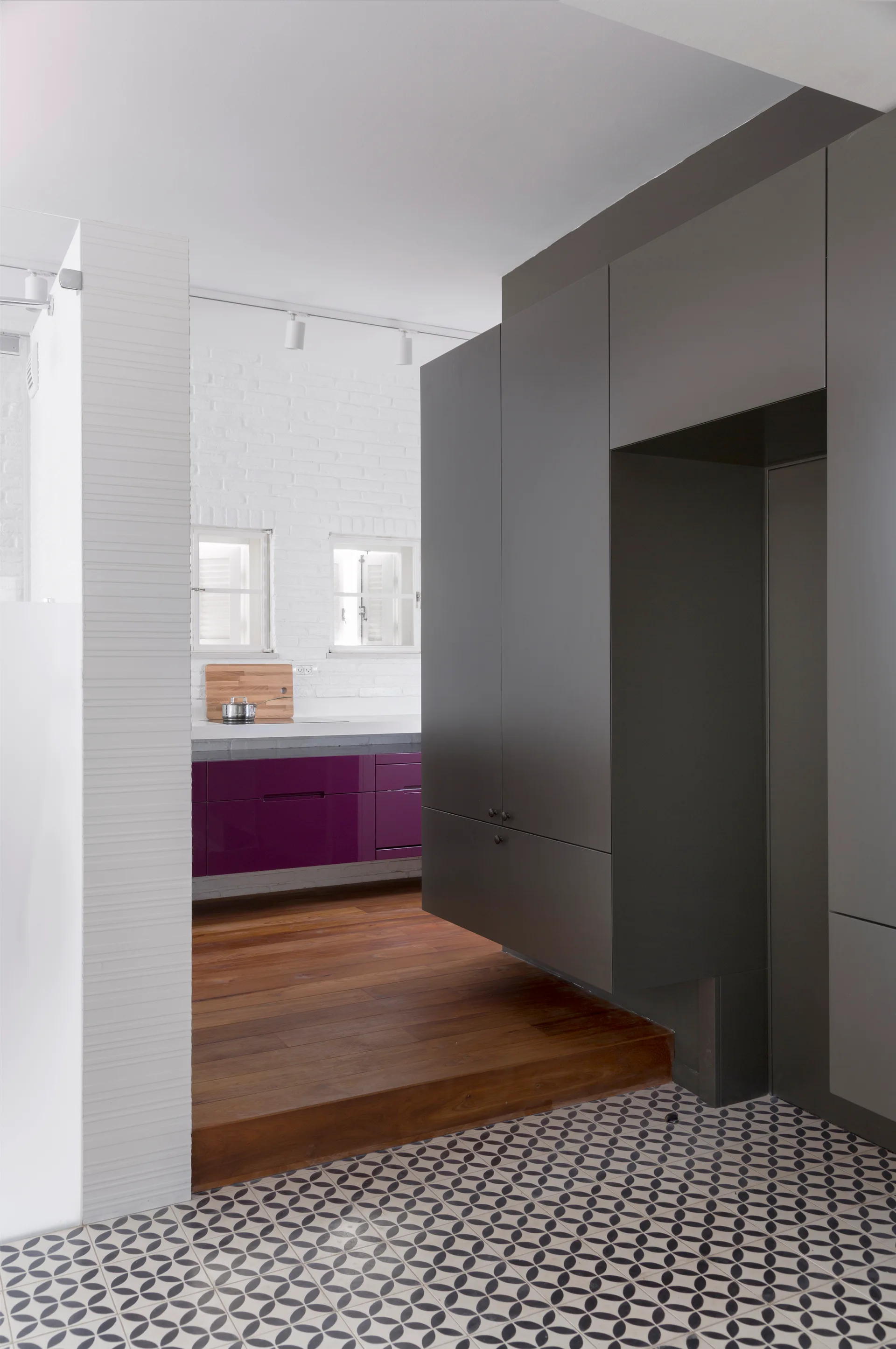 A kitchen features dark grey matte cabinetry, deep purple lower cabinets, a raised wood floor, and geometric black and white tiles.