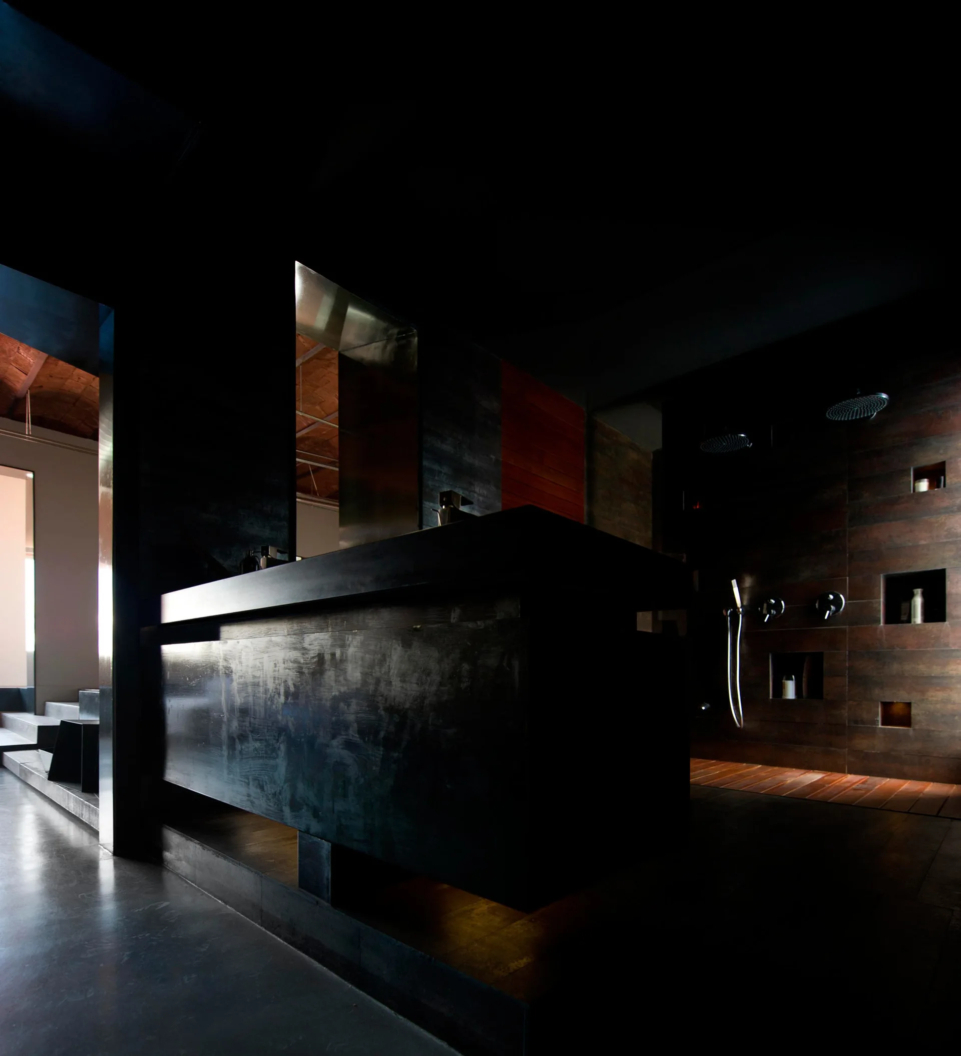 A dark minimalist bathroom featuring a large black vanity, a shower with recessed wall niches, and slatted wood flooring.