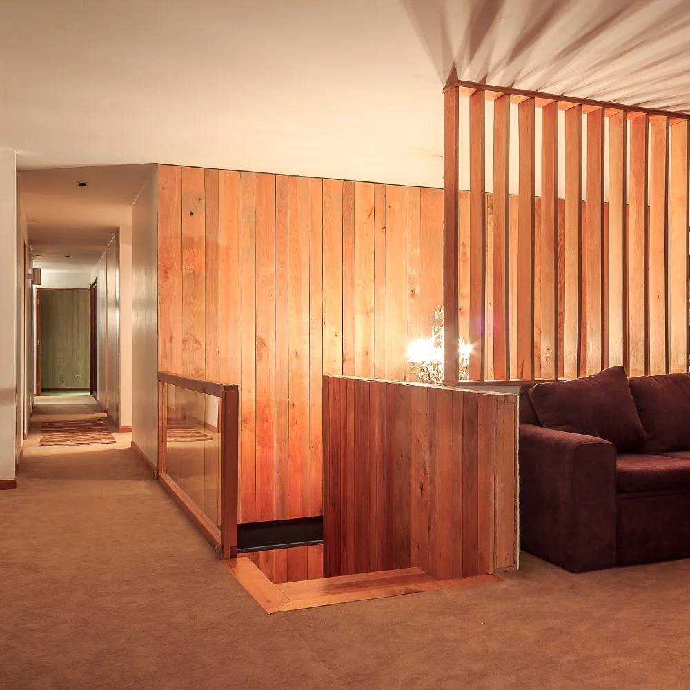 A residential staircase landing features vertical wood plank wall paneling, a wooden slatted partition wall, and a dark brown sofa.
