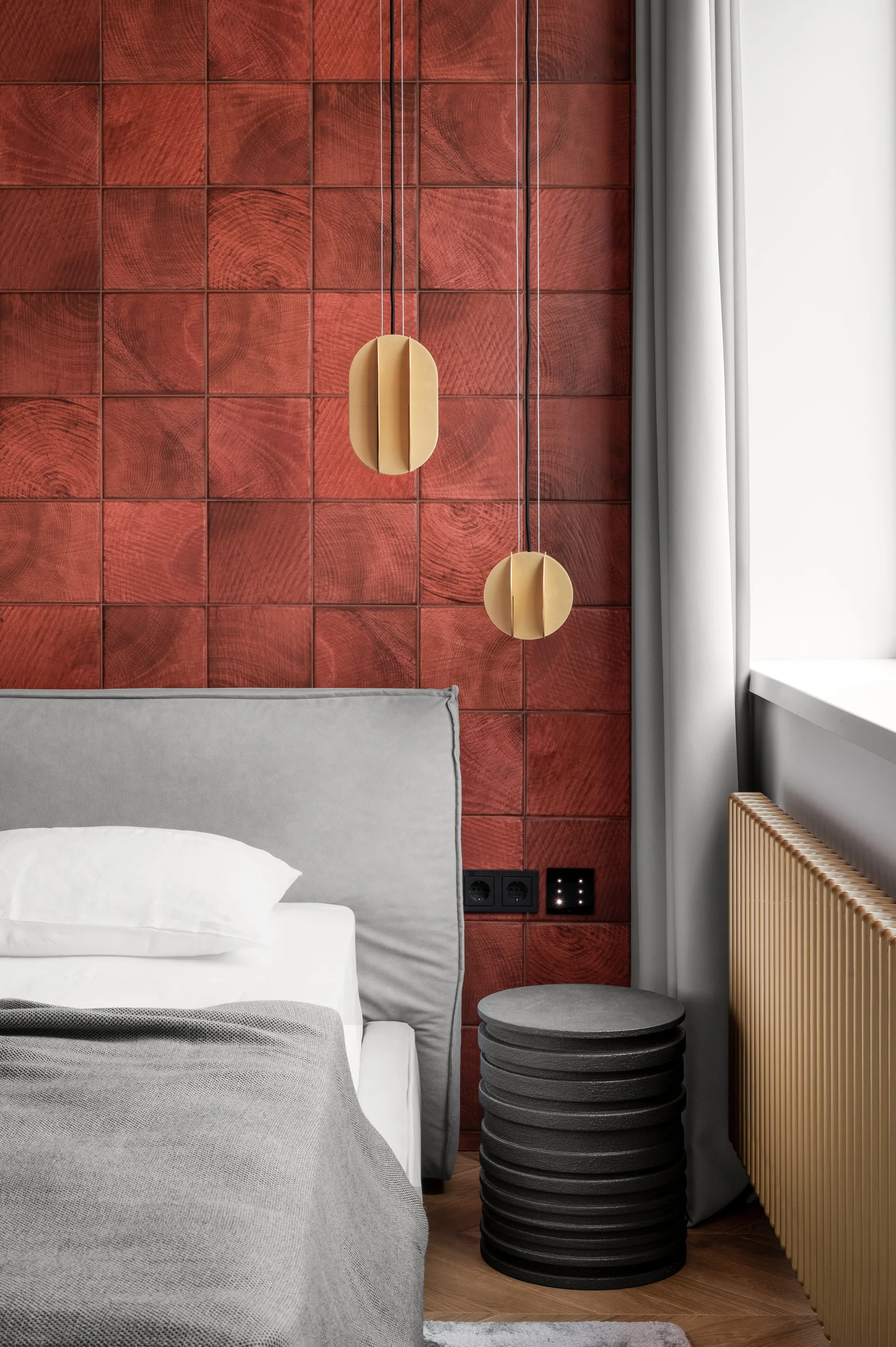 A bedroom corner features a red square-tiled wood accent wall, a grey upholstered bed, and a dark cylindrical bedside table.