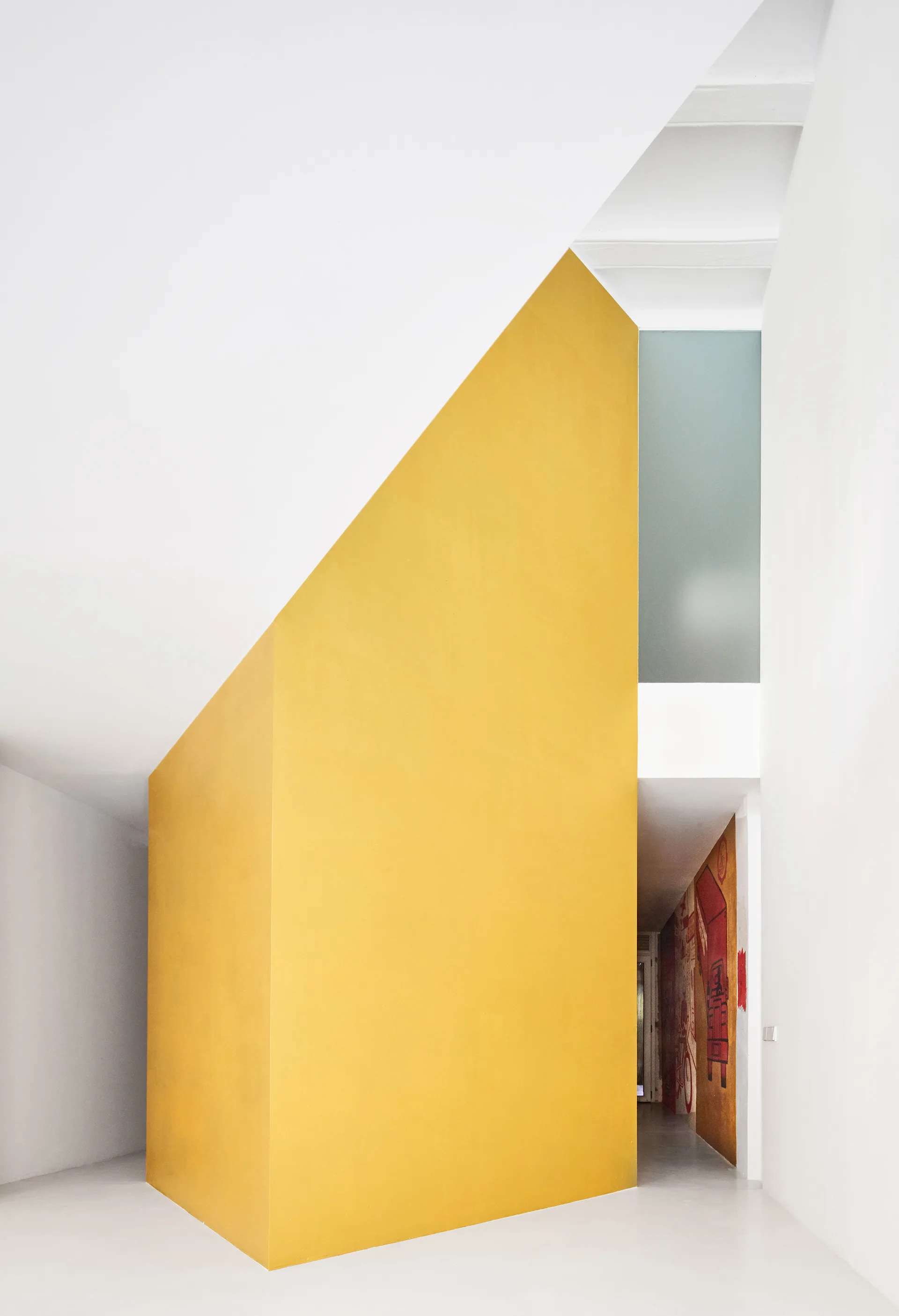 A minimalist hallway featuring a prominent yellow angular accent wall, smooth white floors, and a distant red wall mural.