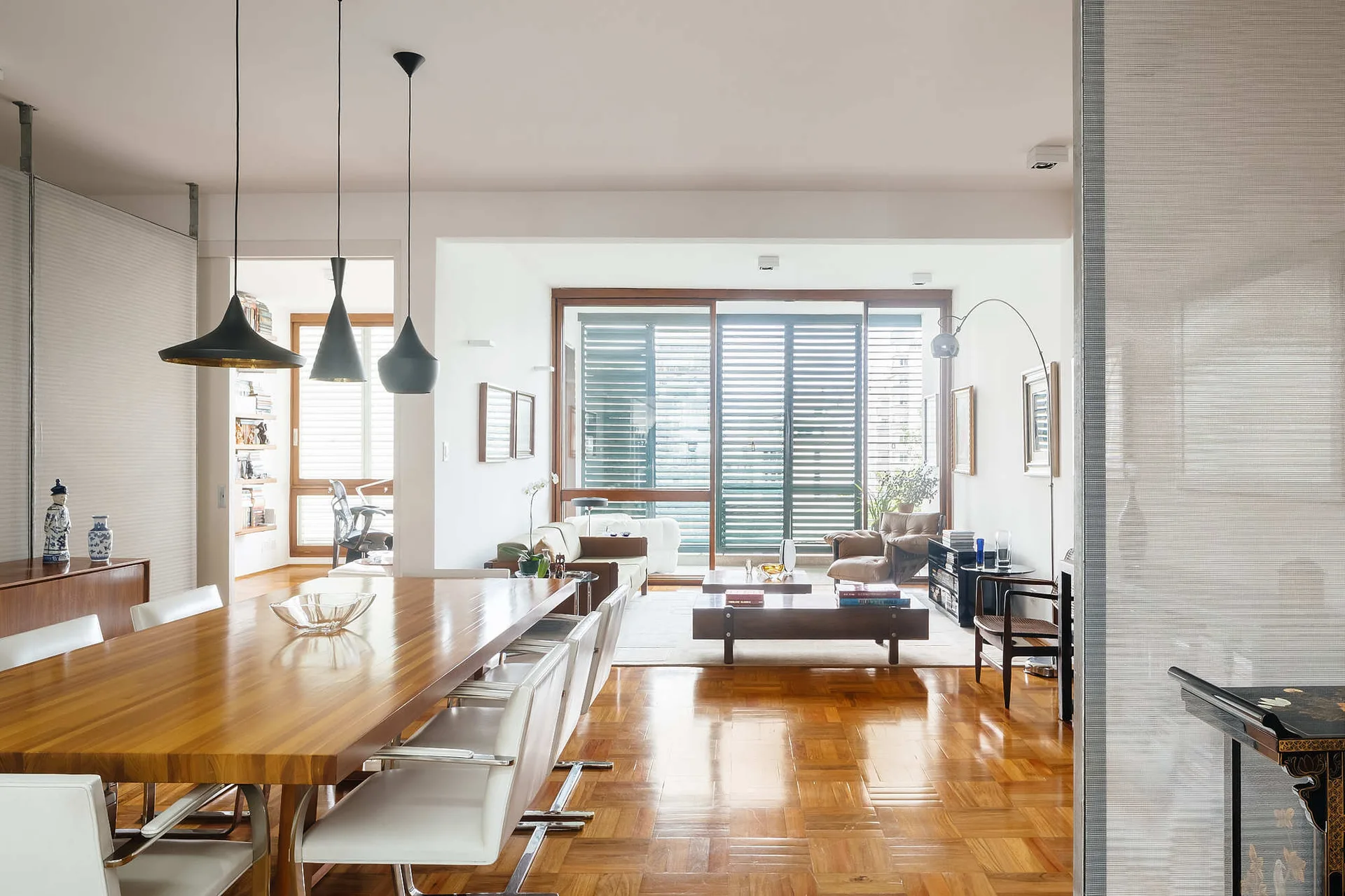 An open-plan living and dining space with a long wood table, white chairs, and a polished parquet wood floor.