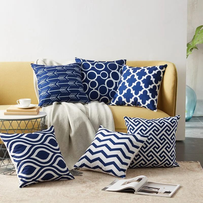 Six navy blue and white patterned throw pillows are arranged on and in front of a mustard yellow sofa.