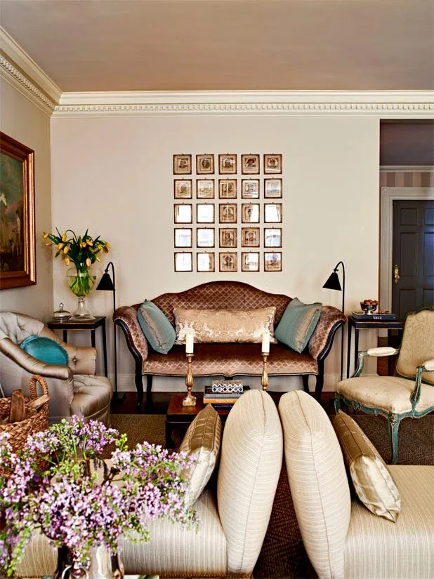 A traditional living room features a patterned sofa flanked by black floor lamps, sitting below a precise grid of small framed pictures.