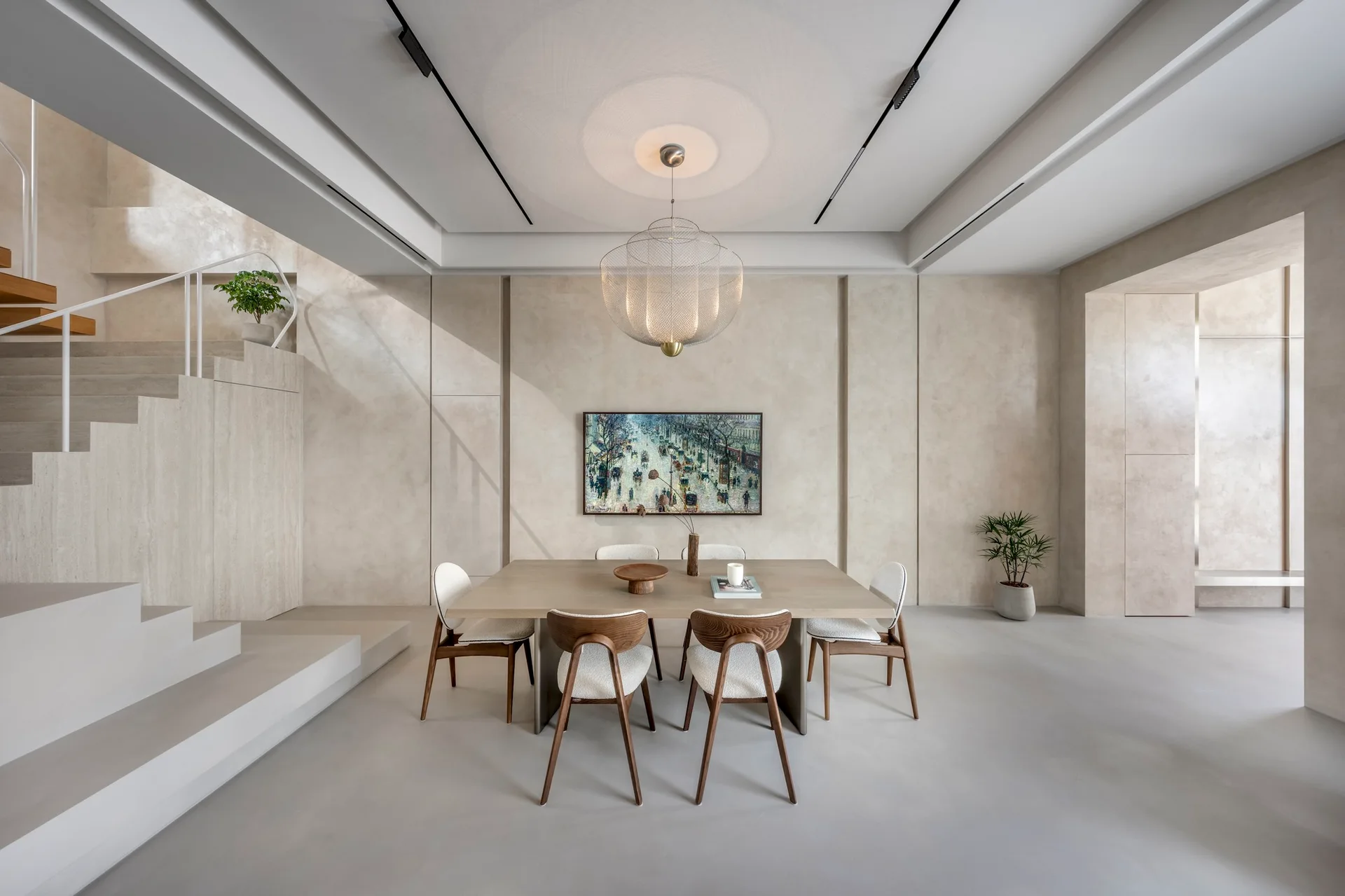 A minimalist dining room featuring a light wood table surrounded by sculptural chairs beneath a mesh pendant light, beside a stone-like staircase.